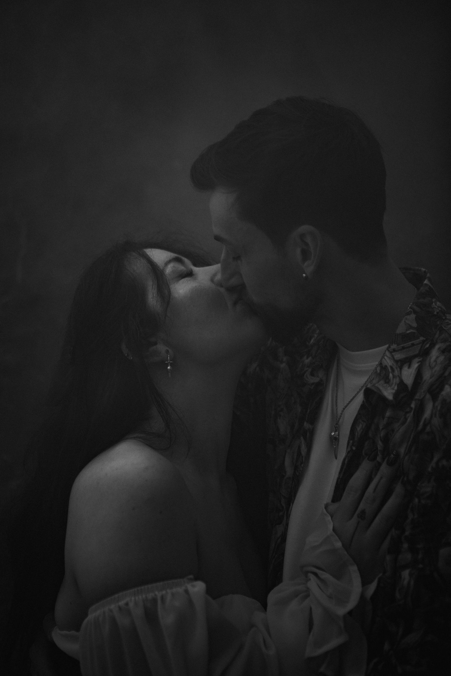 Black and white romantic photo of a couple sharing a tender kiss against a dark moody background.