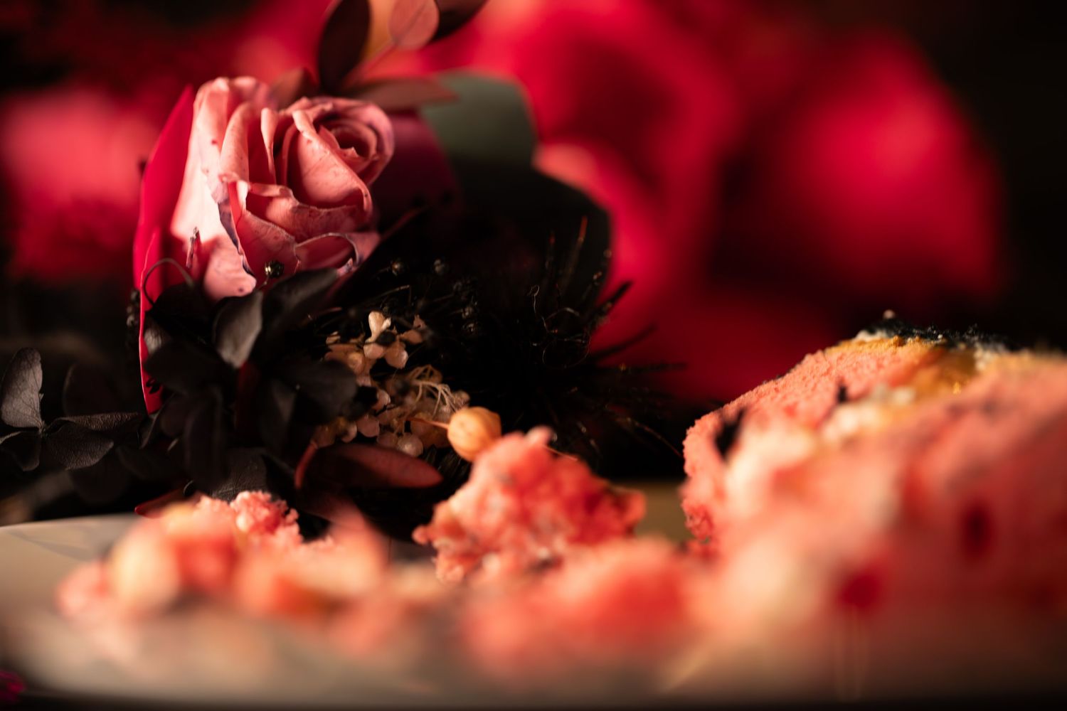 Close-up of deep red roses and dark floral wedding cake decoration with moody lighting.