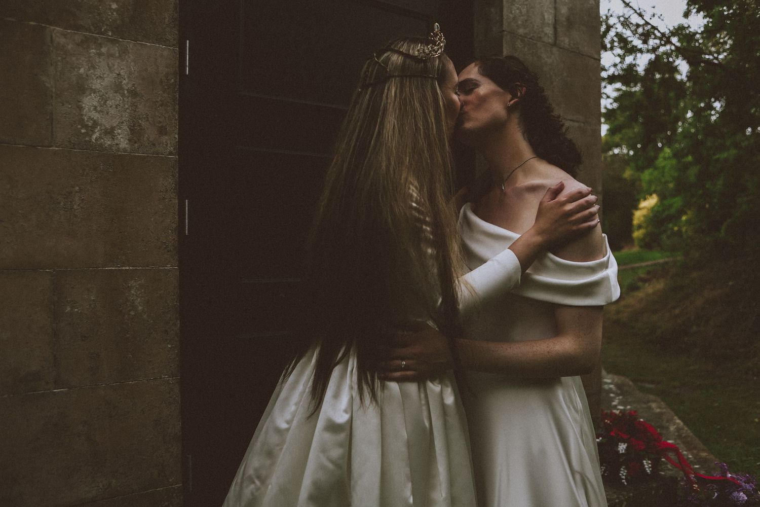 Two brides in white gowns share an intimate embrace in a romantic outdoor wedding photo.