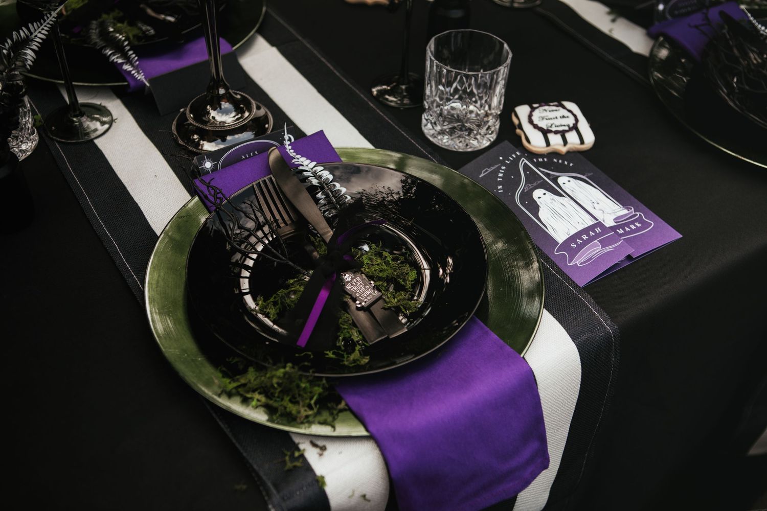 Elegant Halloween table setting with black plates, purple napkins, and gothic decor on a dark tablecloth.