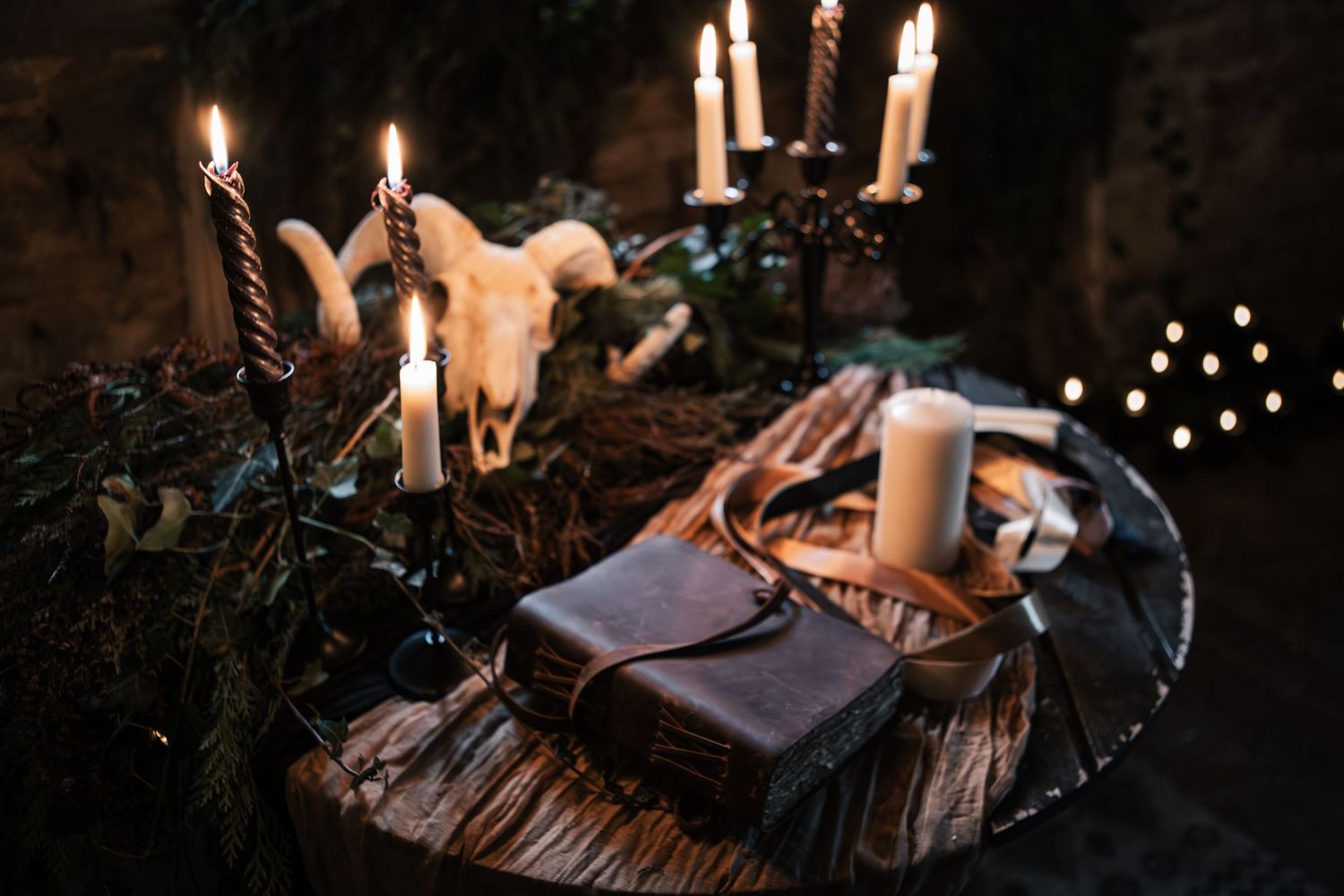 Mystical altar with candles, animal skull, and leather journal on a wooden surface in a dark, moody setting.
