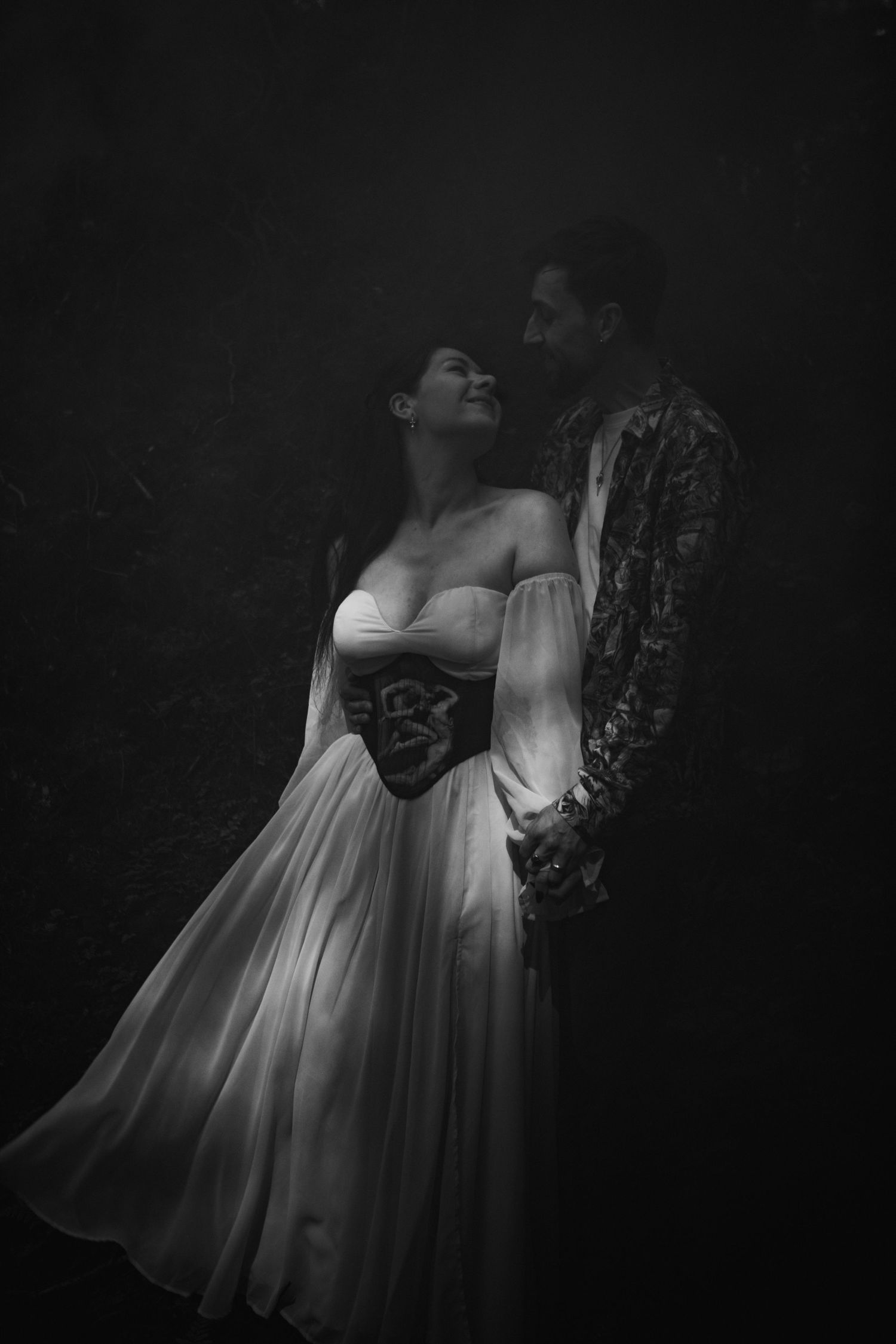 Black and white romantic portrait of couple embracing, woman in elegant corset wedding gown.