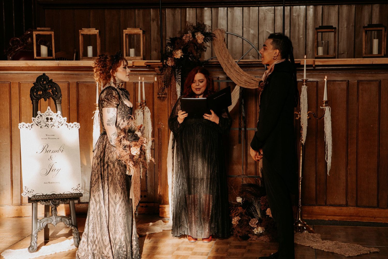 Gothic wedding ceremony with tattooed bride in lace gown at rustic wooden venue altar.
