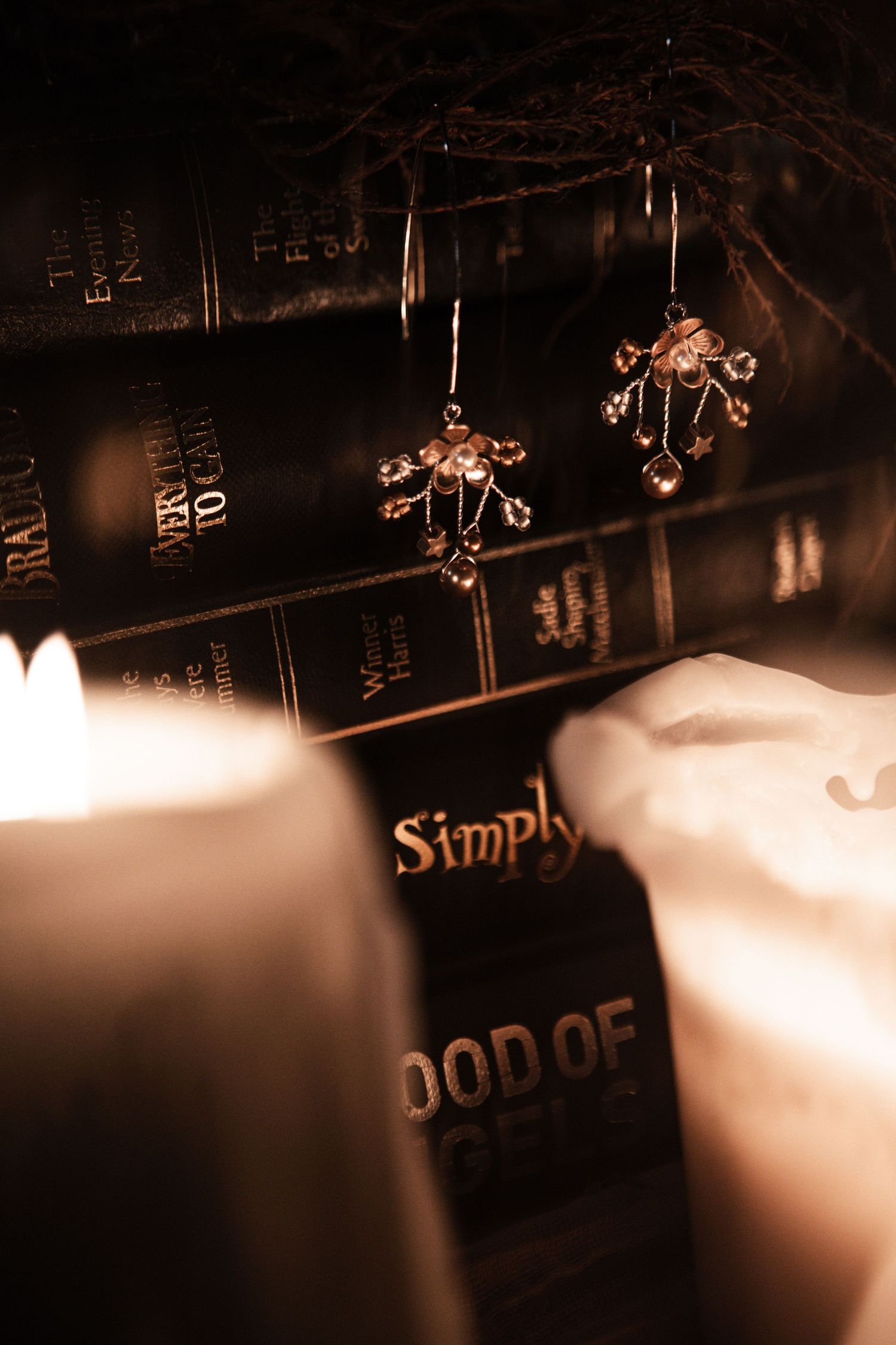Crystal cross earrings displayed among dark antique books by candlelight in a gothic styled flat lay.