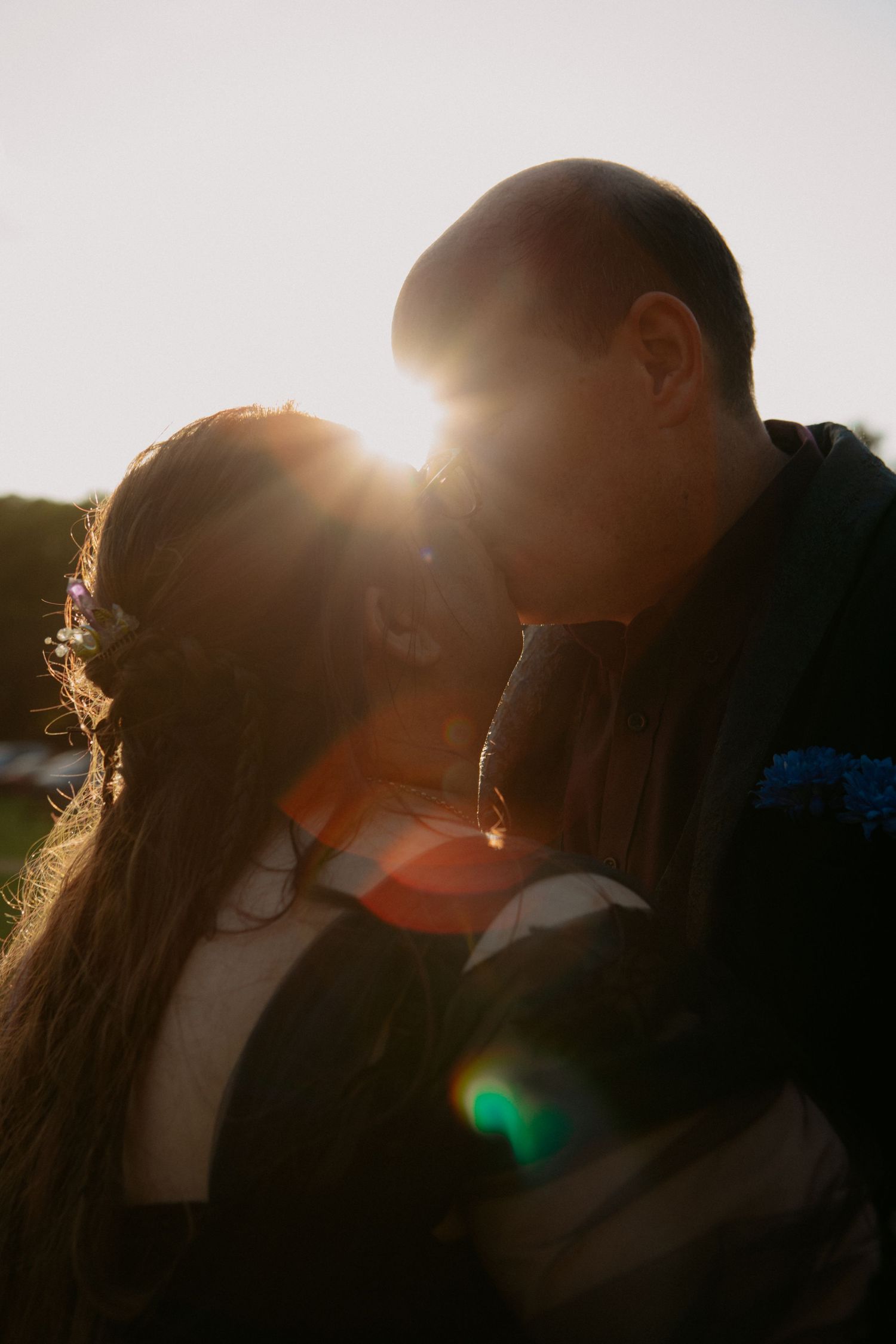 Couple sharing a romantic kiss backlit by golden sunset light, creating a beautiful lens flare effect outdoors.
