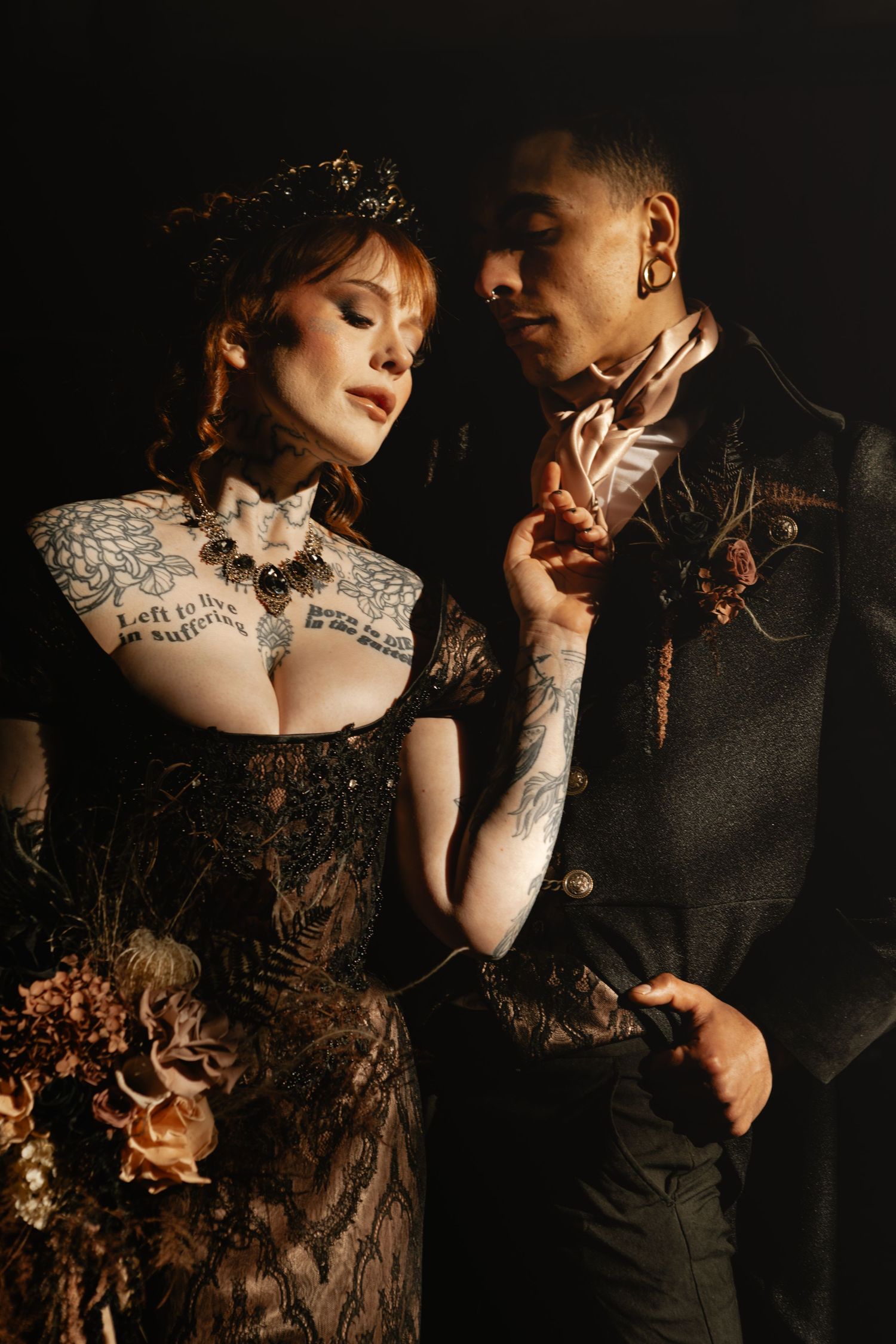 Tattooed gothic bride in black lace gown with groom touching her chest tattoos tenderly.