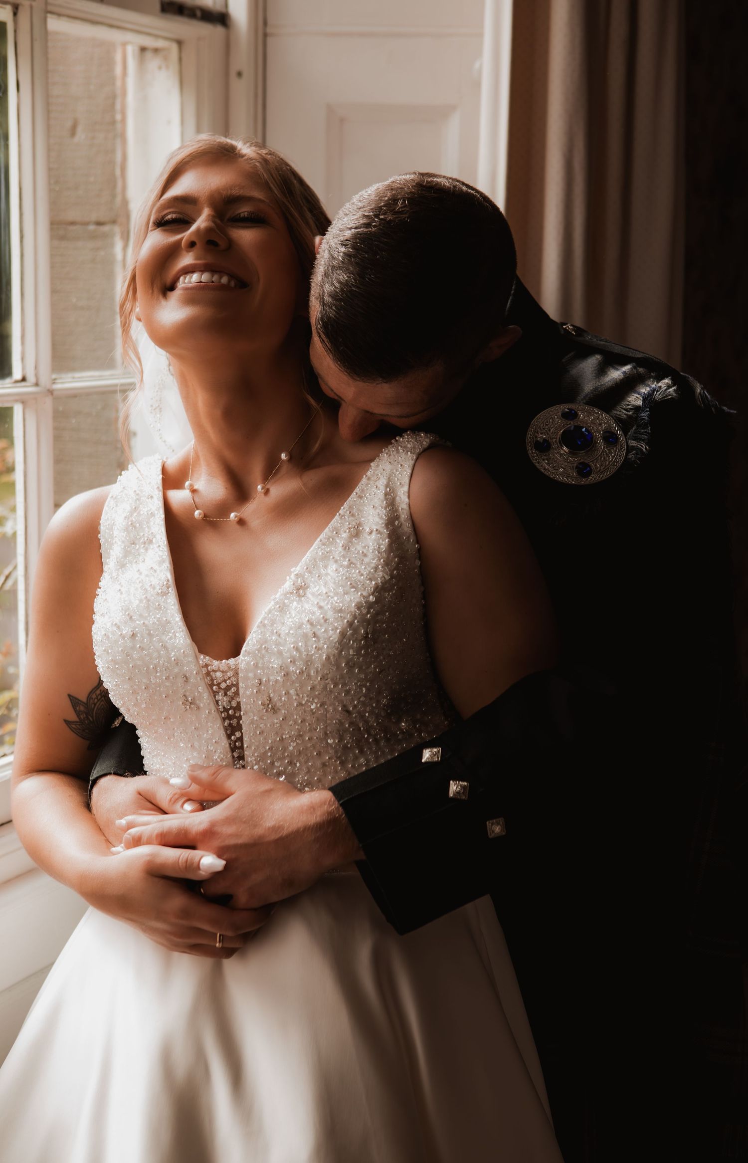 A tender moment between newlyweds as they embrace by a window, with the bride wearing a beautiful white lace wedding gown.