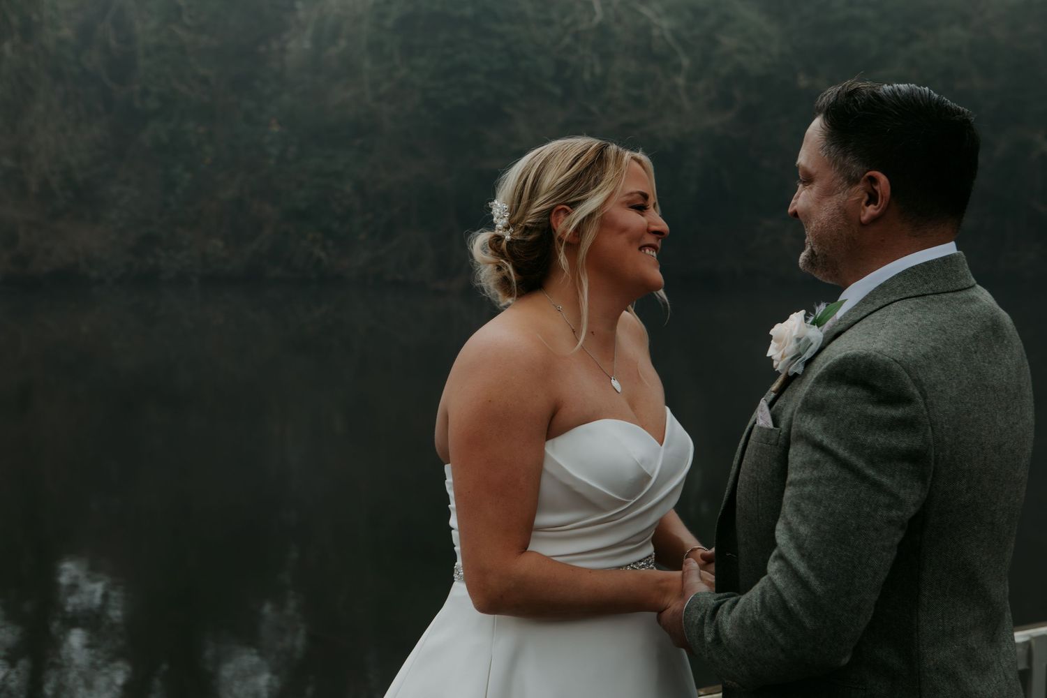 A romantic wedding couple shares an intimate moment in their formal attire against a misty outdoor backdrop.