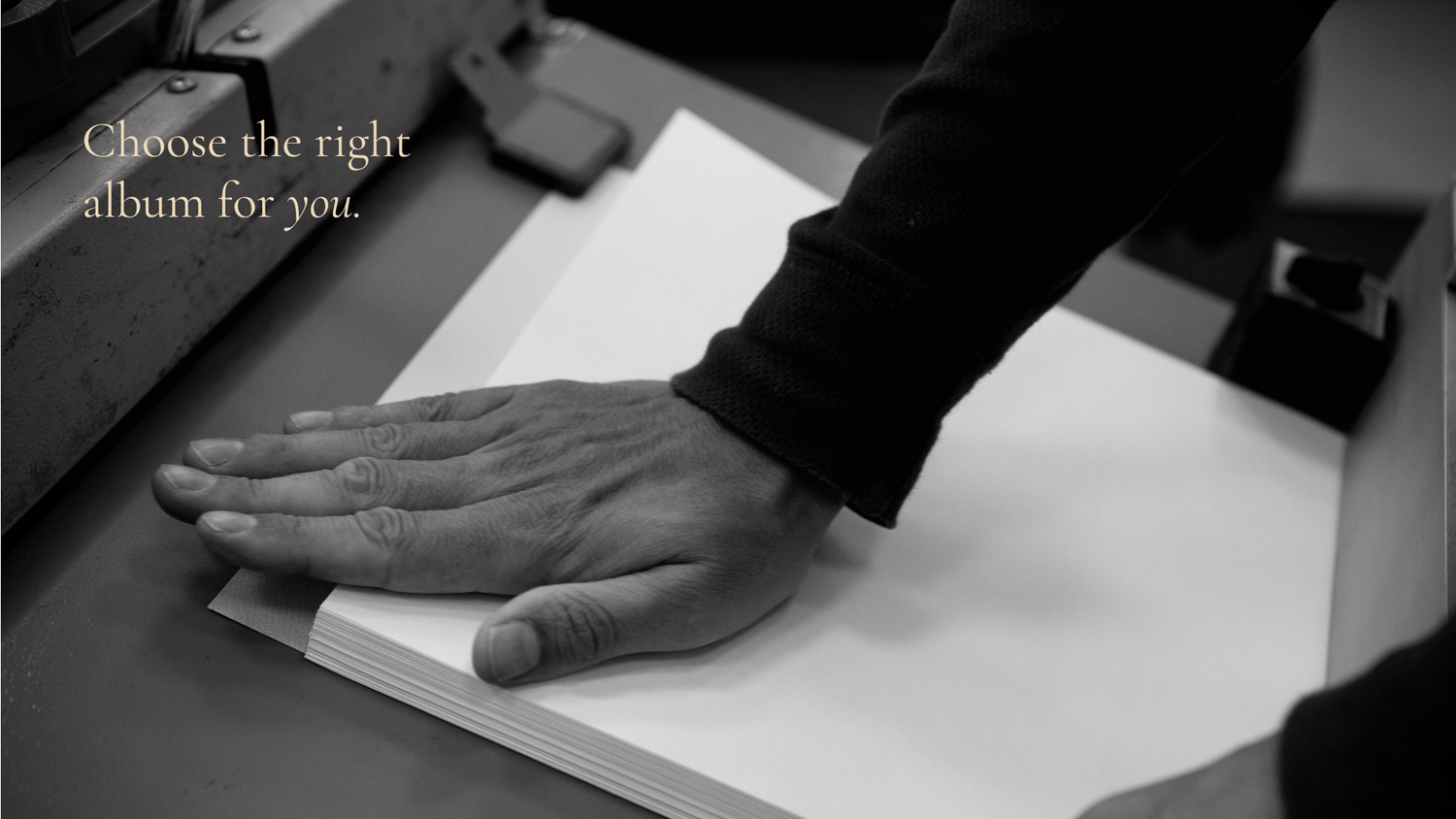 A black and white close-up photo shows a hand resting on white paper against a dark background.