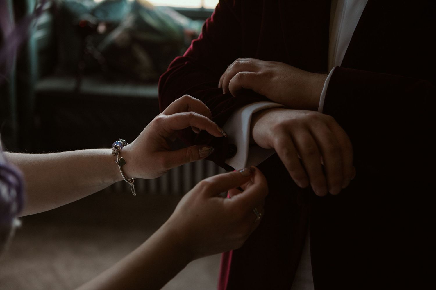 Hands adjusting a white pocket square on a dark suit jacket during wedding preparations.