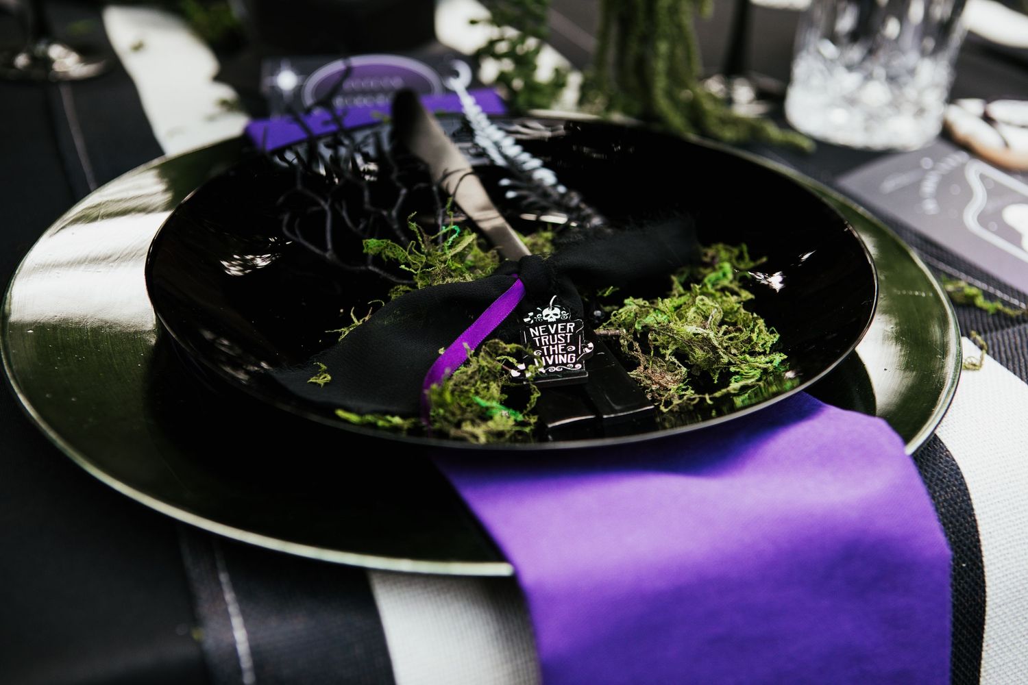 Black plate with moss and purple ribbon table setting, elegant gothic wedding decor.