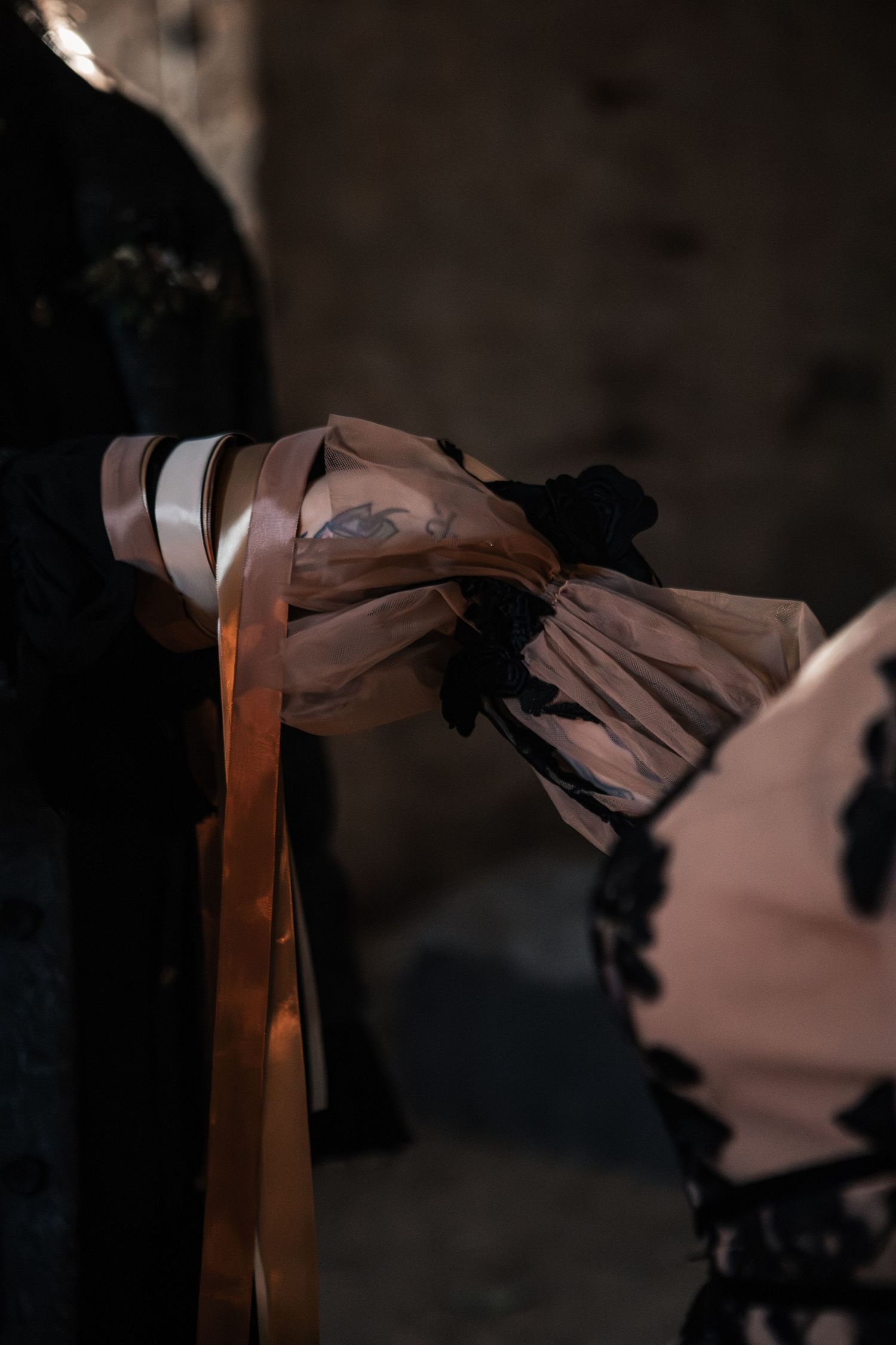 Close-up of gothic bride's tattooed hand tied with copper ribbon in sheer black lace sleeve.