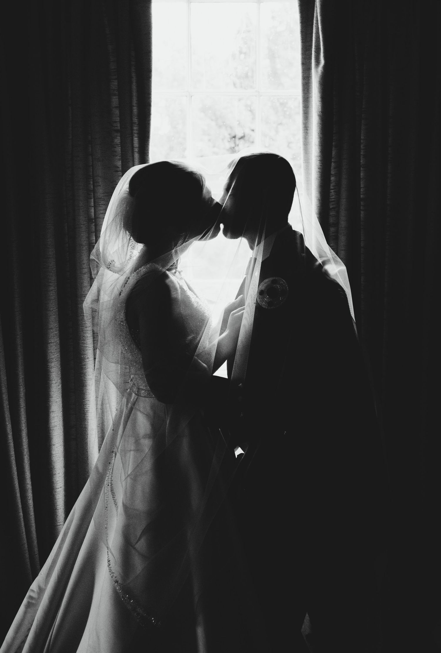 A silhouetted wedding couple shares a tender moment backlit by a window.