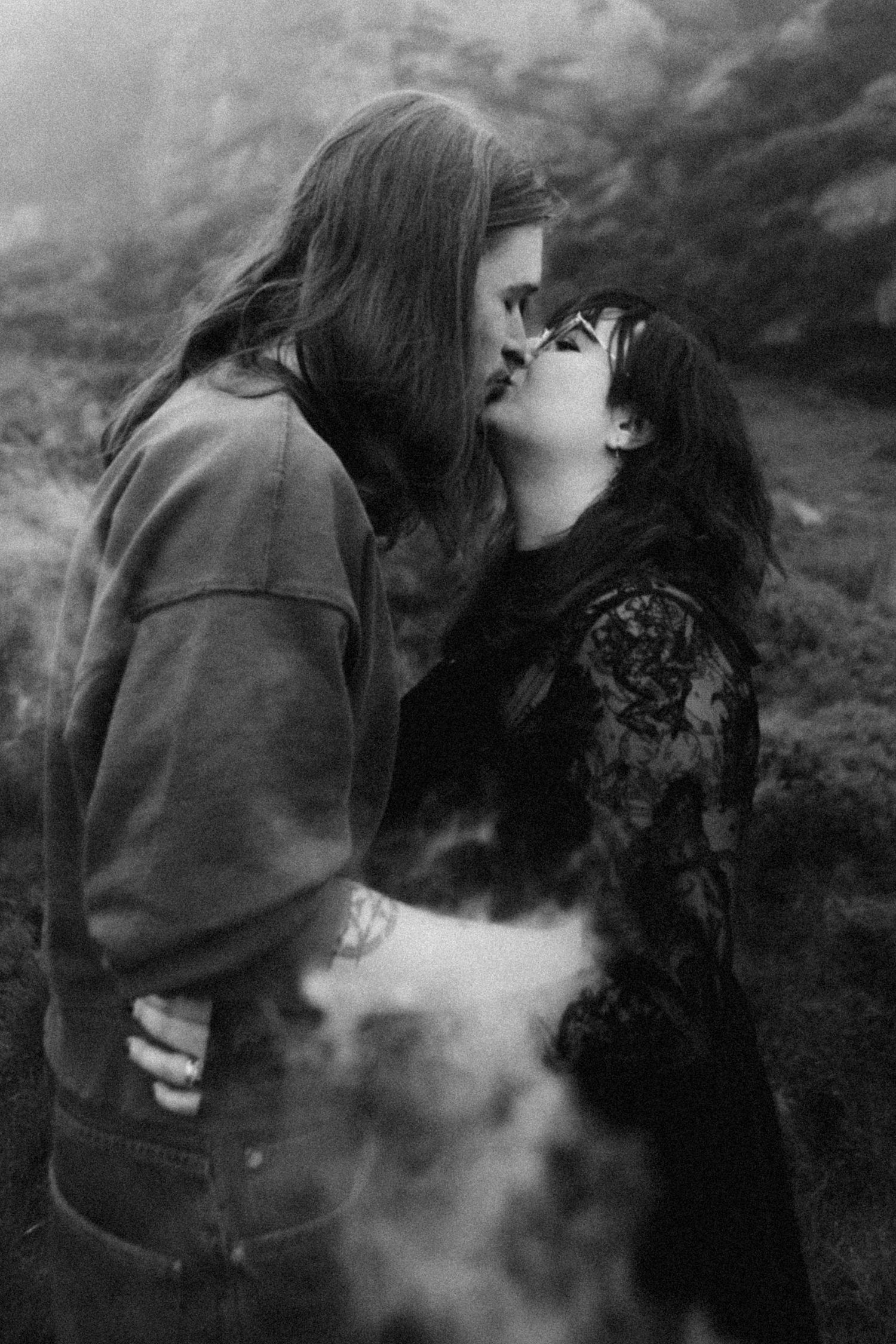Black and white photo of a couple sharing a kiss with smoke swirling around them outdoors.
