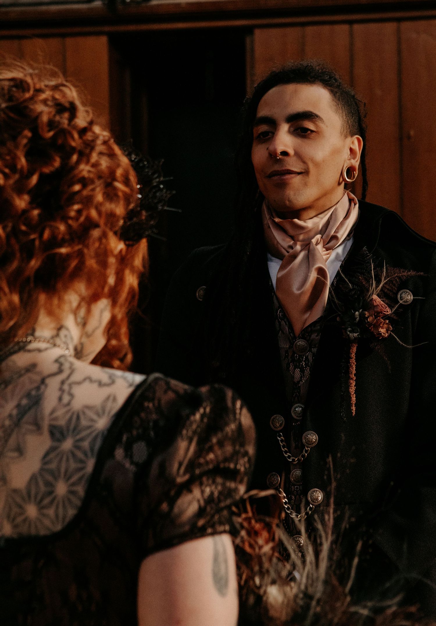 Groom in black velvet suit with gold earring and cravat sharing intimate moment with tattooed bride.