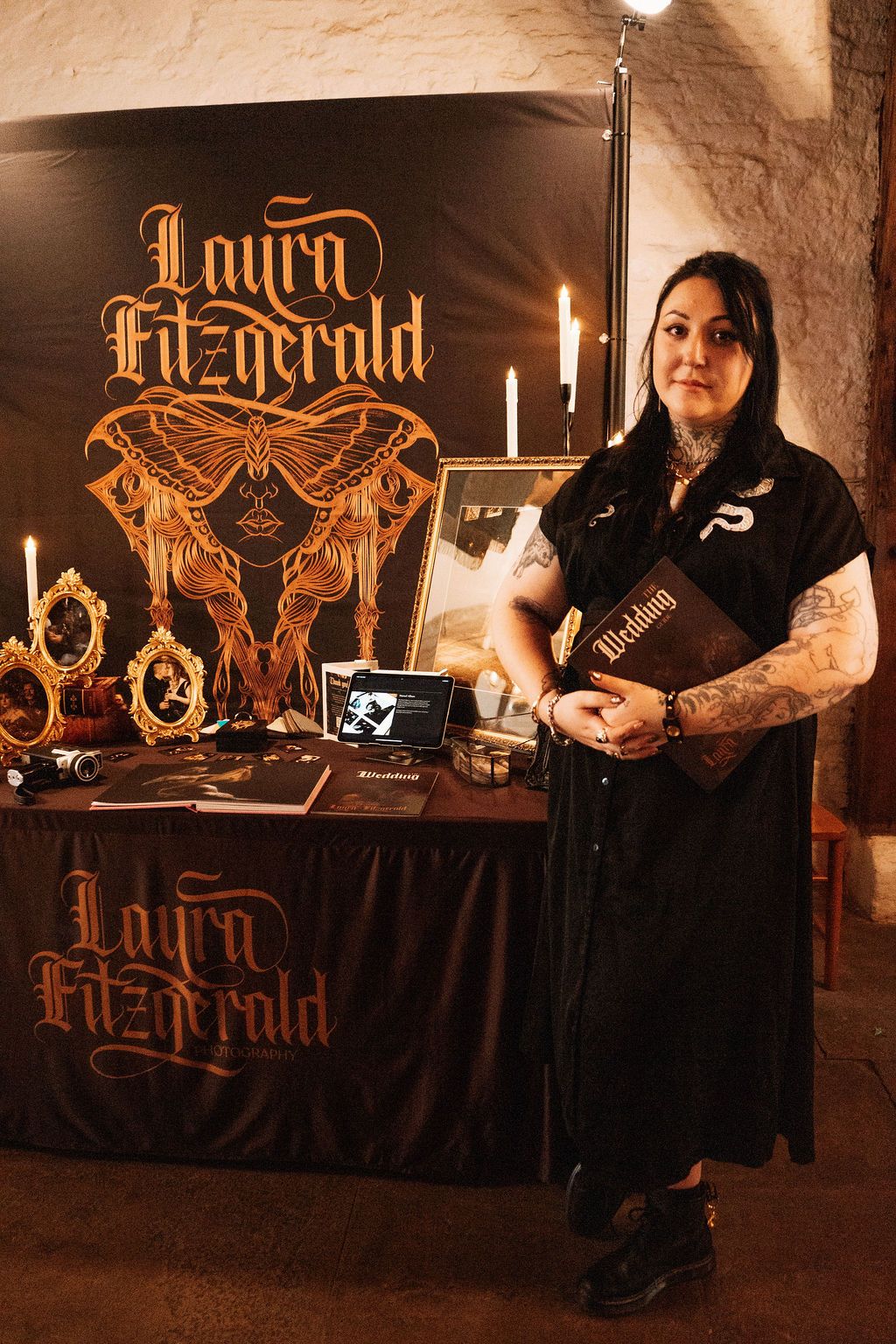 Tattoo artist Laura Fitzgerald stands at branded merchandise table with candles.
