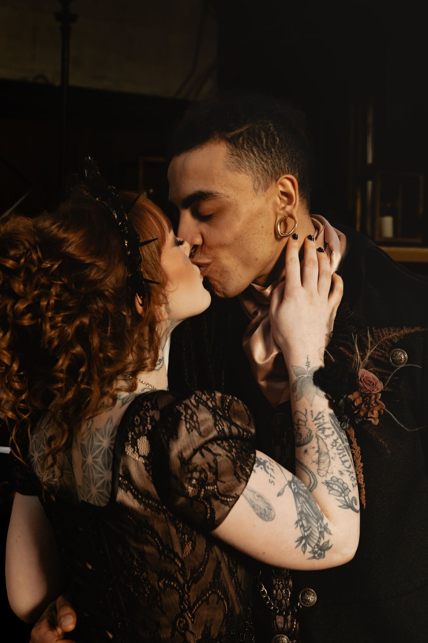 Tattooed couple sharing a romantic kiss in a dark, moody setting, with the woman in black lace.