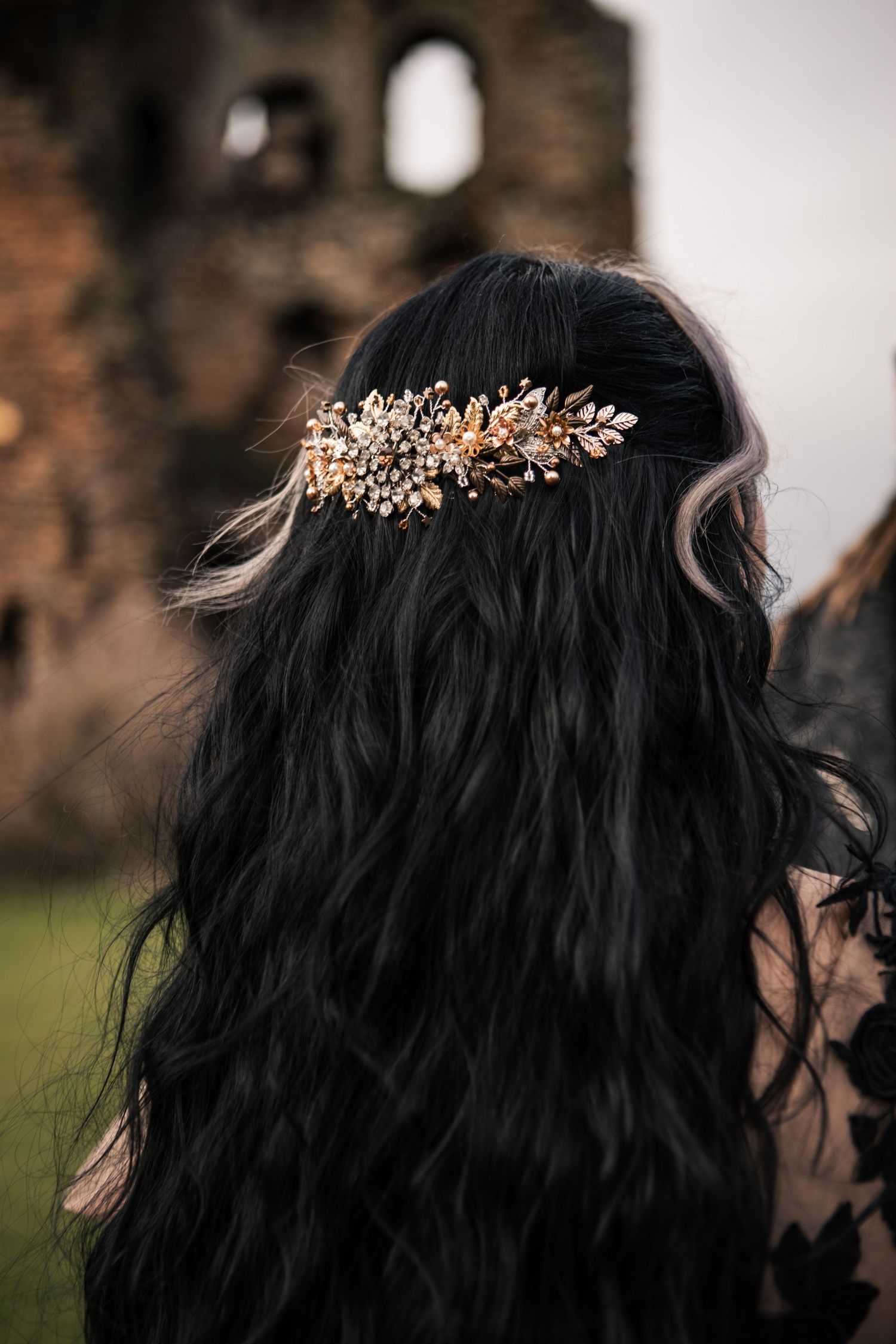 Back view of dark wavy hair adorned with ornate gold floral hair comb at castle ruins.
