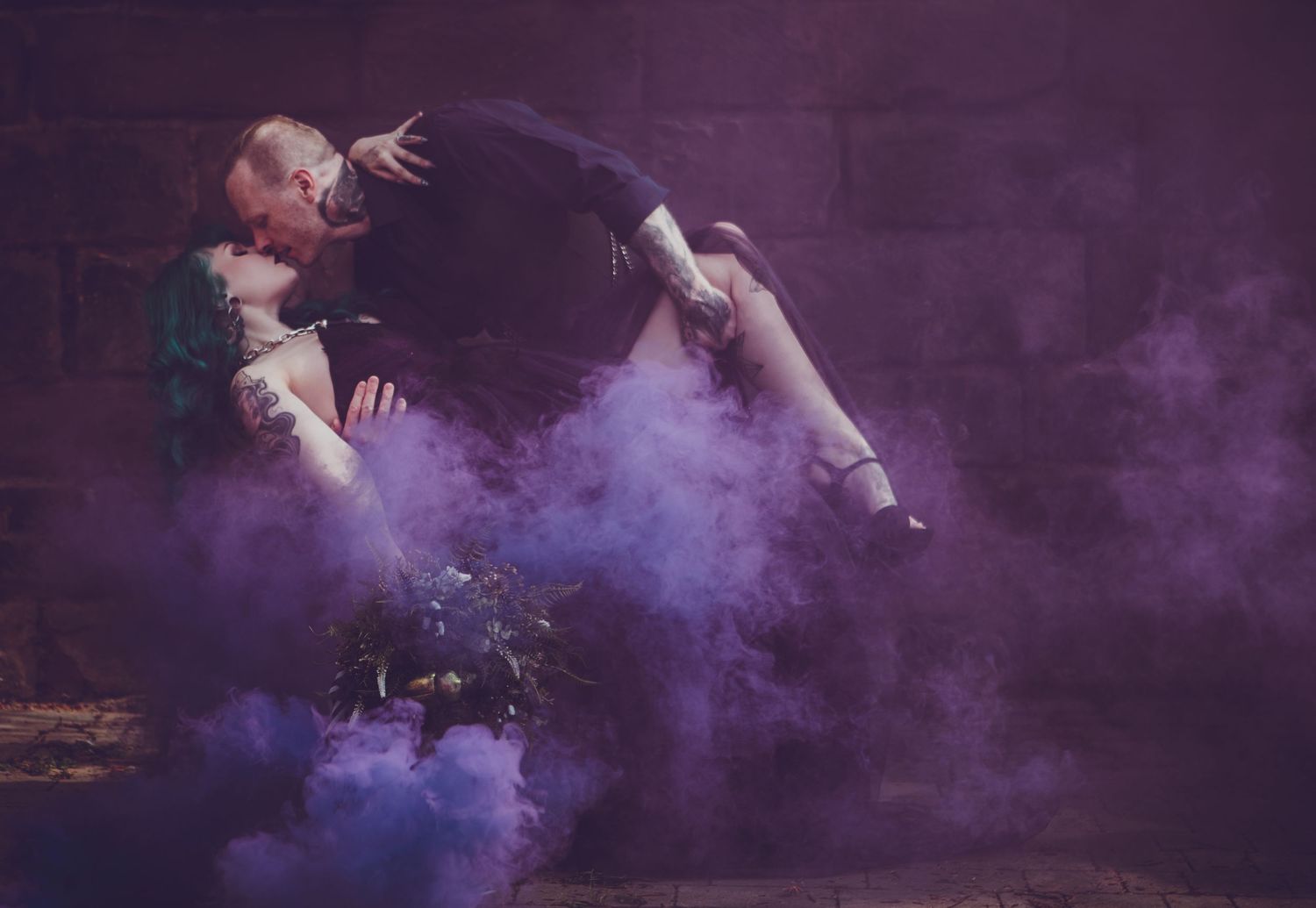 Two dancers perform a dramatic lift surrounded by purple smoke against a dark stone wall.