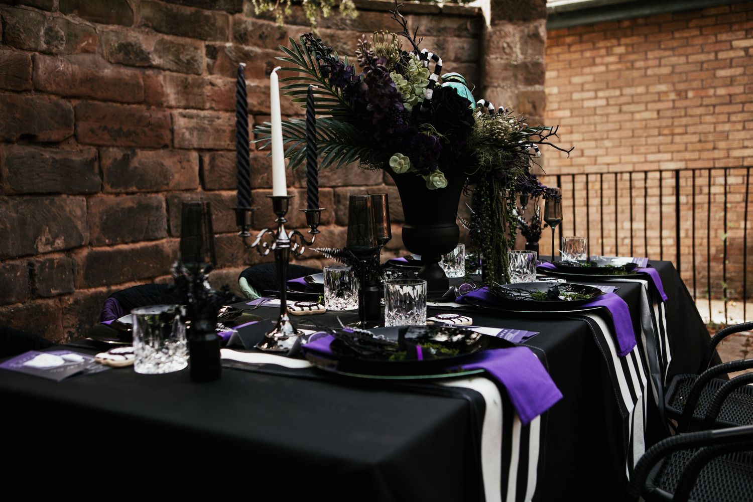 Gothic wedding tablescape with black tablecloth, purple runner, black and white stripes, candles, and dark floral centerpiece.