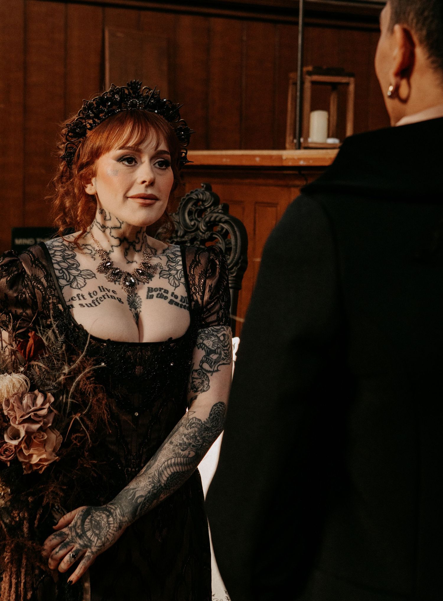 Heavily tattooed bride in black gothic lace wedding dress with ornate black crown during ceremony.