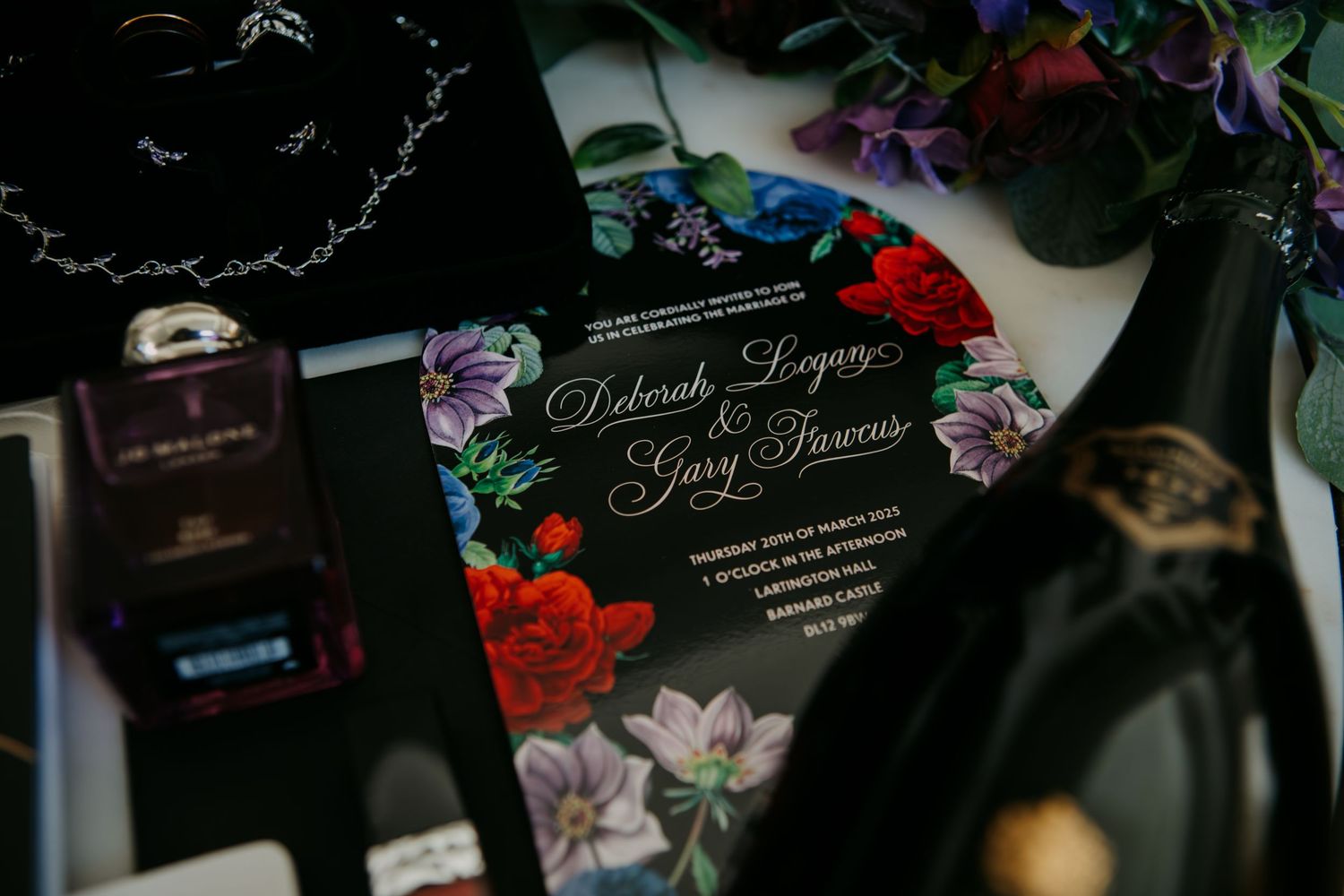 Dark floral wedding invitation for Deborah Logery and Gary Faveons with vibrant red and purple flowers on black background.