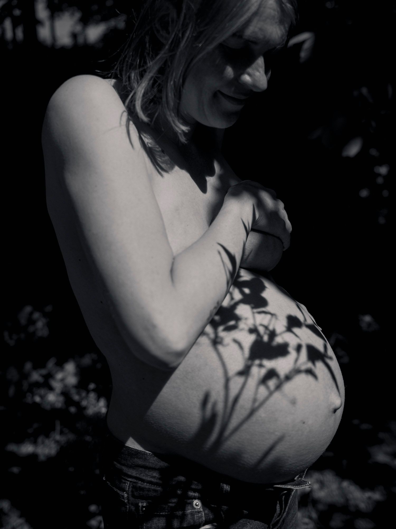 Black and white photo of a pregnant woman outdoors with flower shadows cast across her bare belly.
