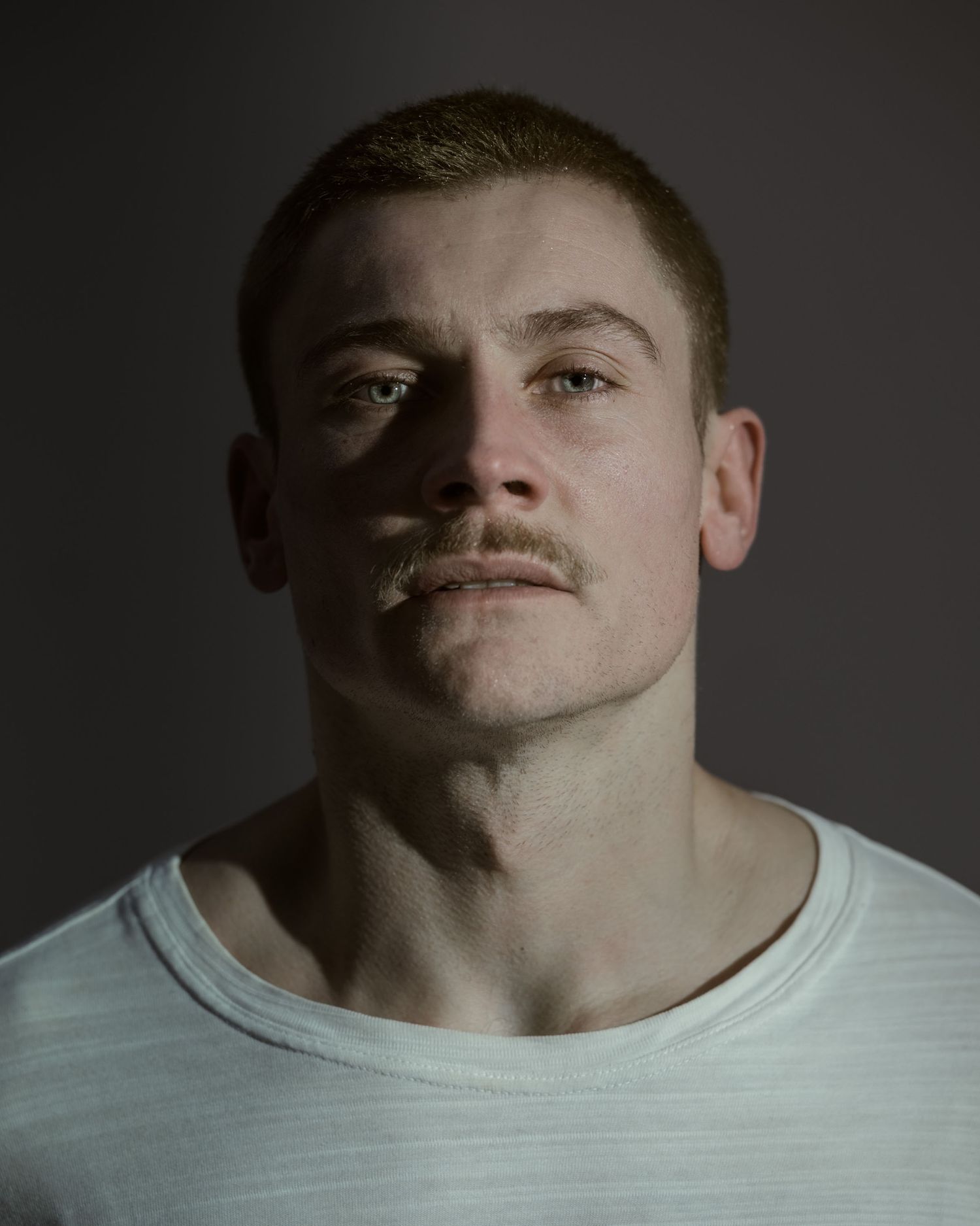 Young muscular man with short hair and mustache wearing a white t-shirt, dramatic studio portrait photography.