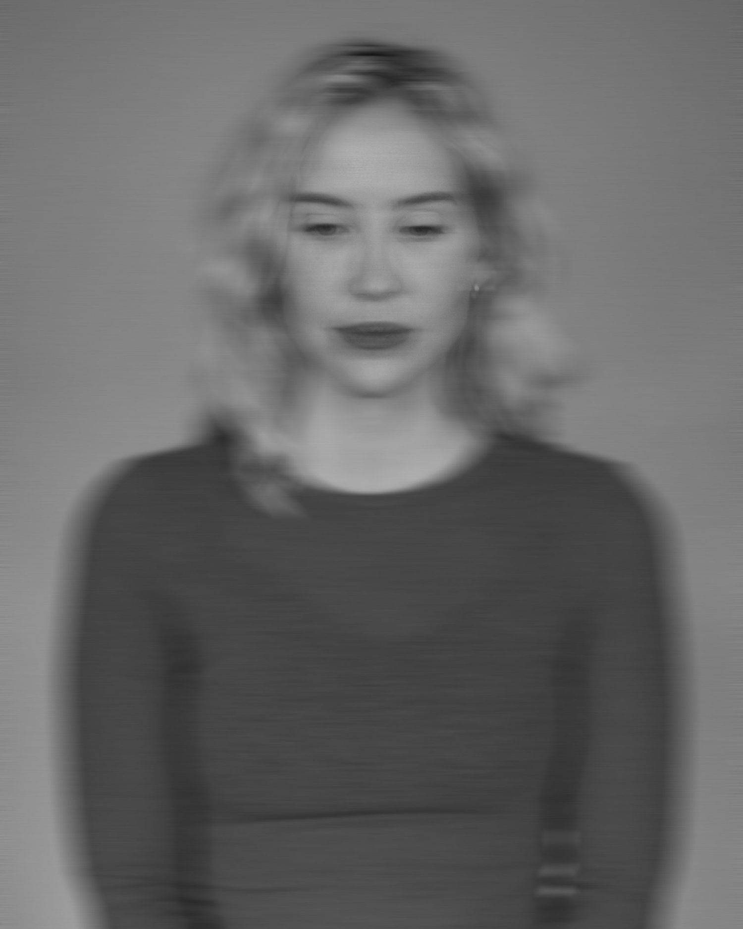 Black and white portrait of a young blonde woman in a striped top, looking down with a contemplative expression.