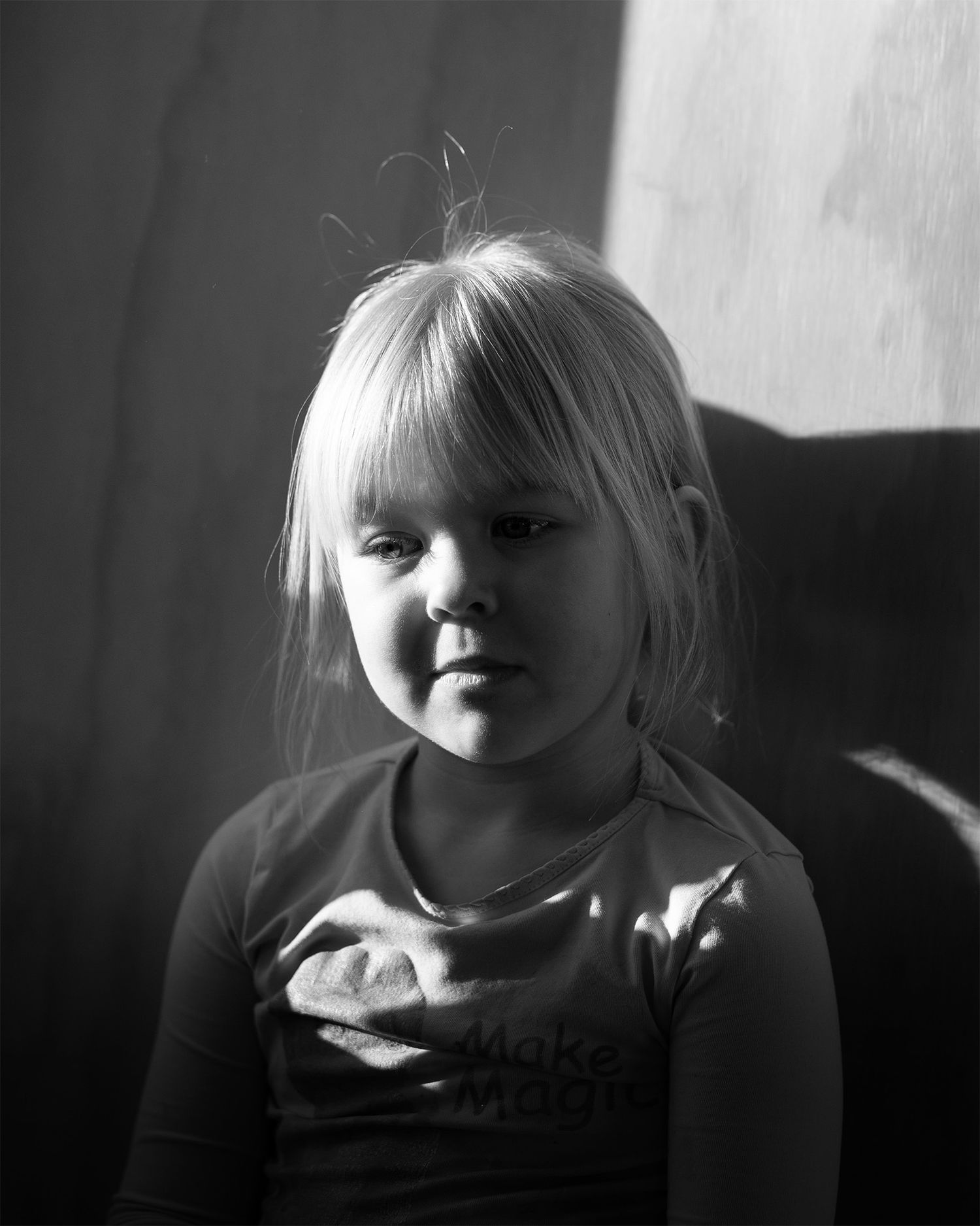 Black and white portrait of a young blonde girl wearing a shirt, illuminated by soft natural light.