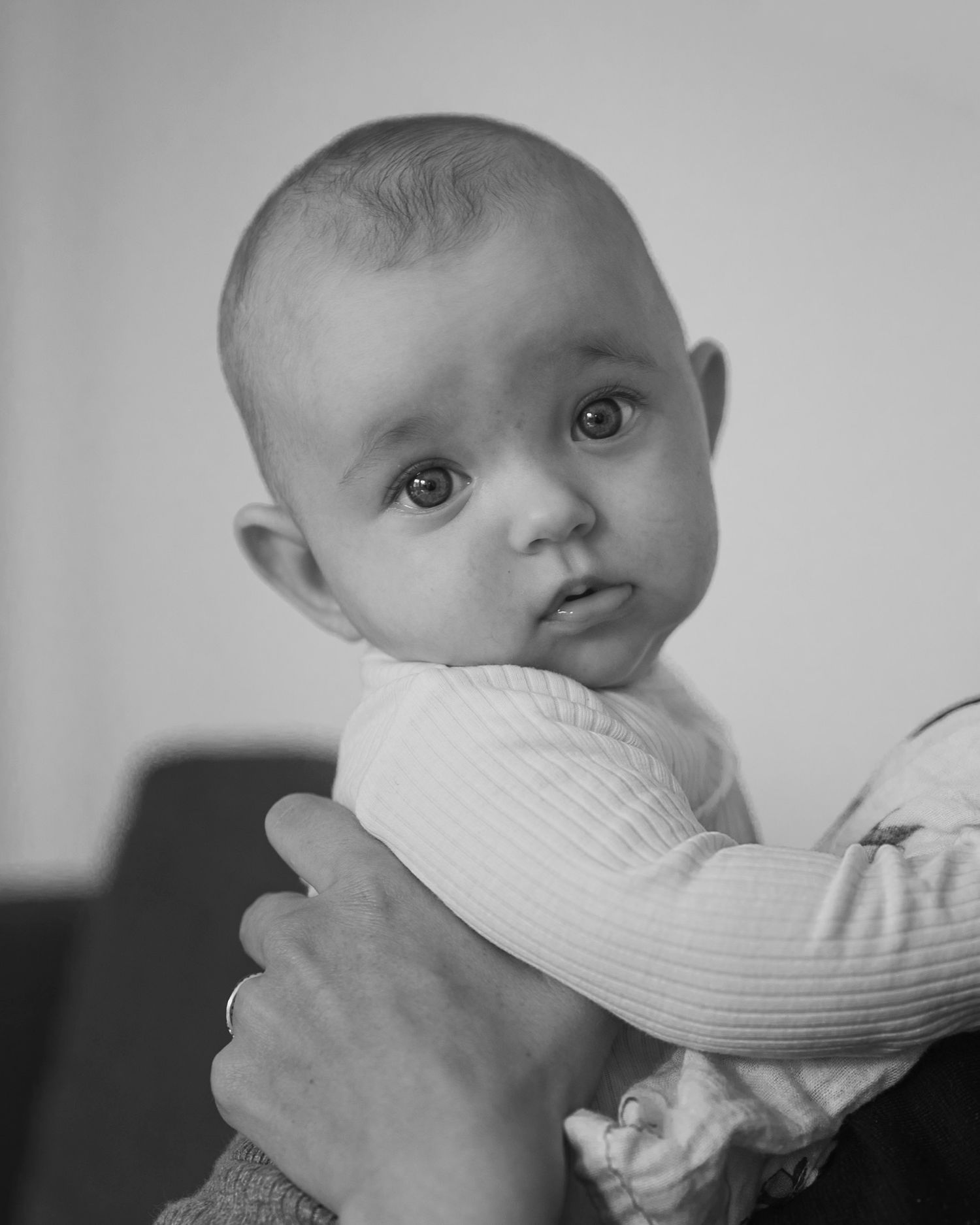 Black and white photo of an alert baby being held by adult hands, wearing a ribbed onesie.