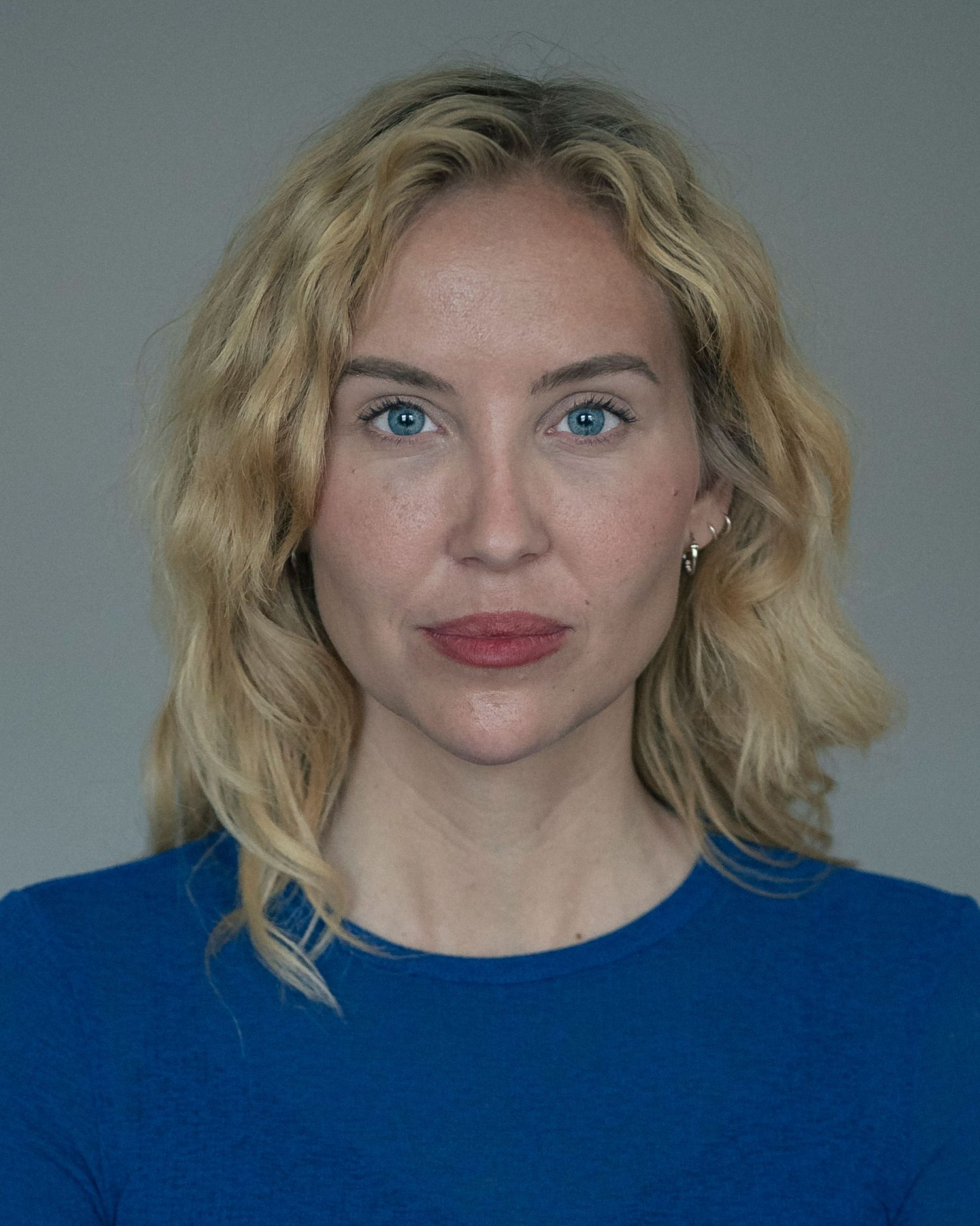 Blonde woman with blue eyes wearing a blue top, headshot photo with neutral gray background.