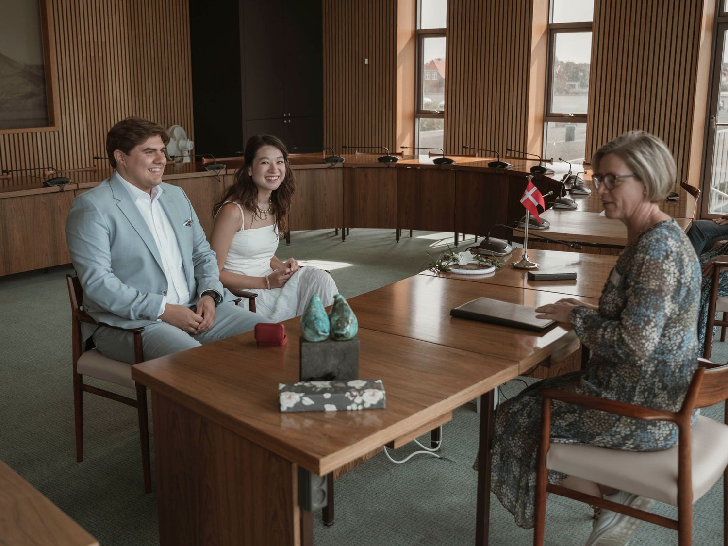 Couple meeting with wedding planner at wooden table in room with large windows.