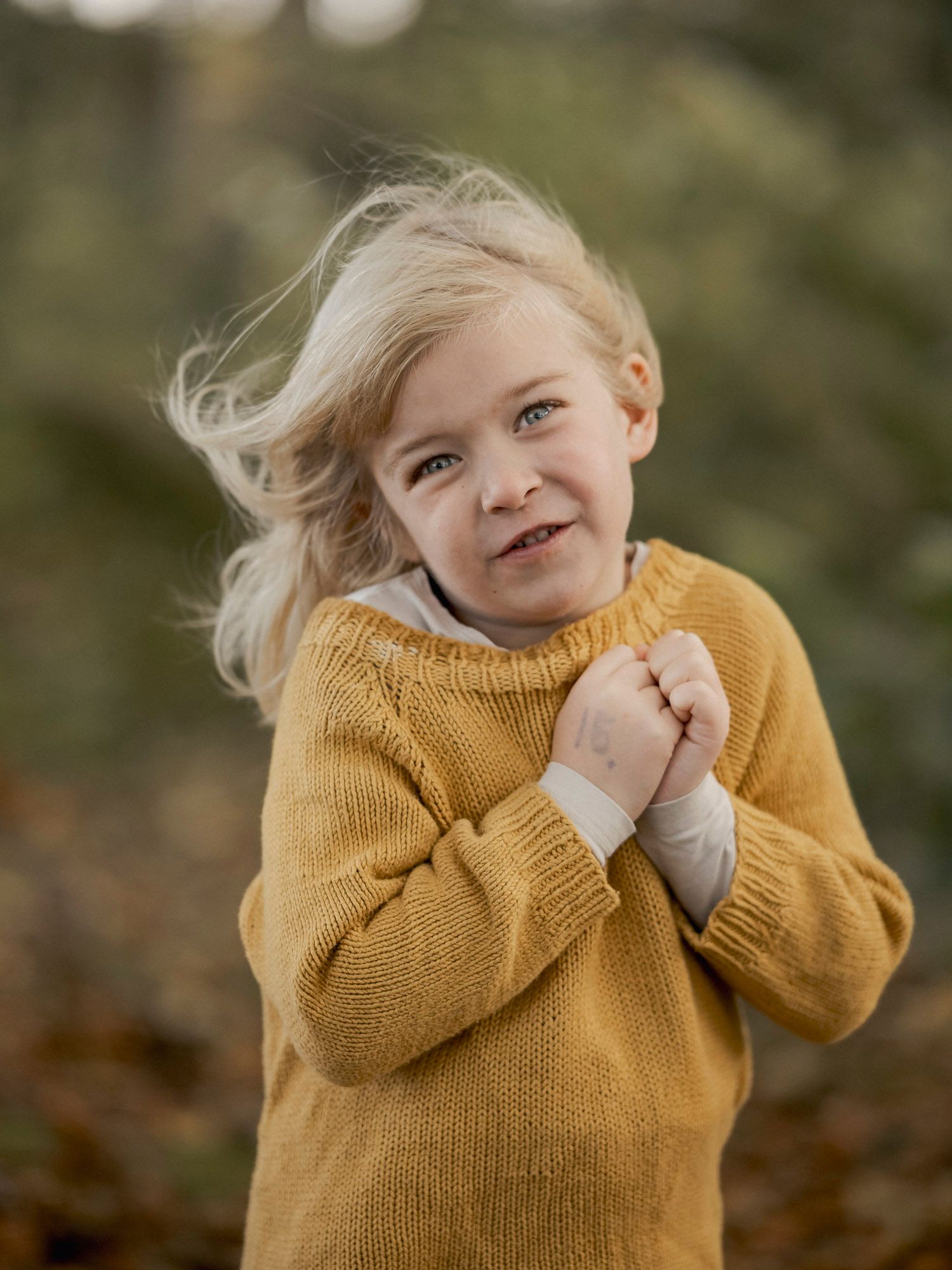 Smiling young girl with blonde hair wearing a mustard yellow knit sweater outdoors in autumn.