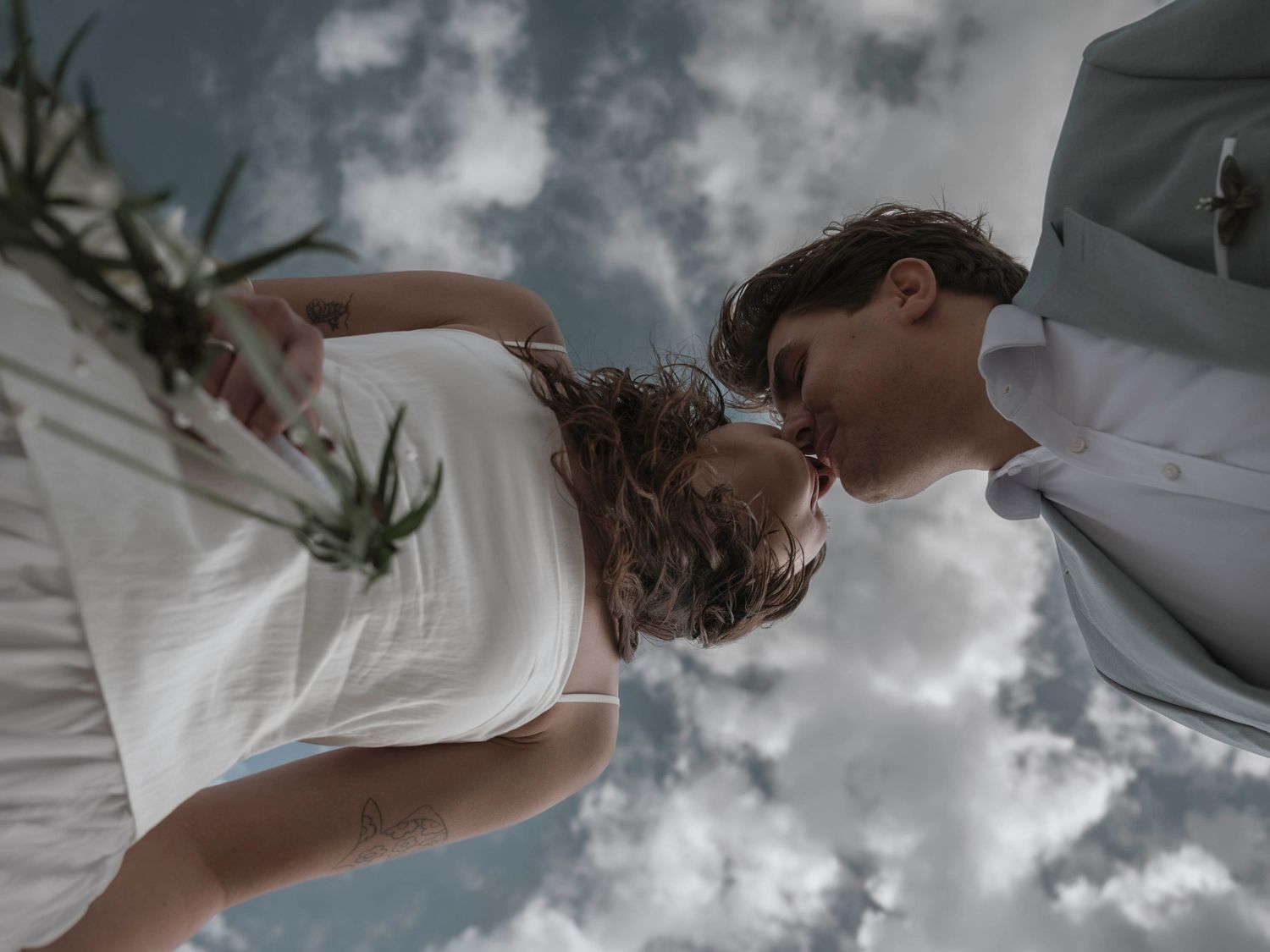 Artistic upward angle photo of a couple embracing against cloudy sky.