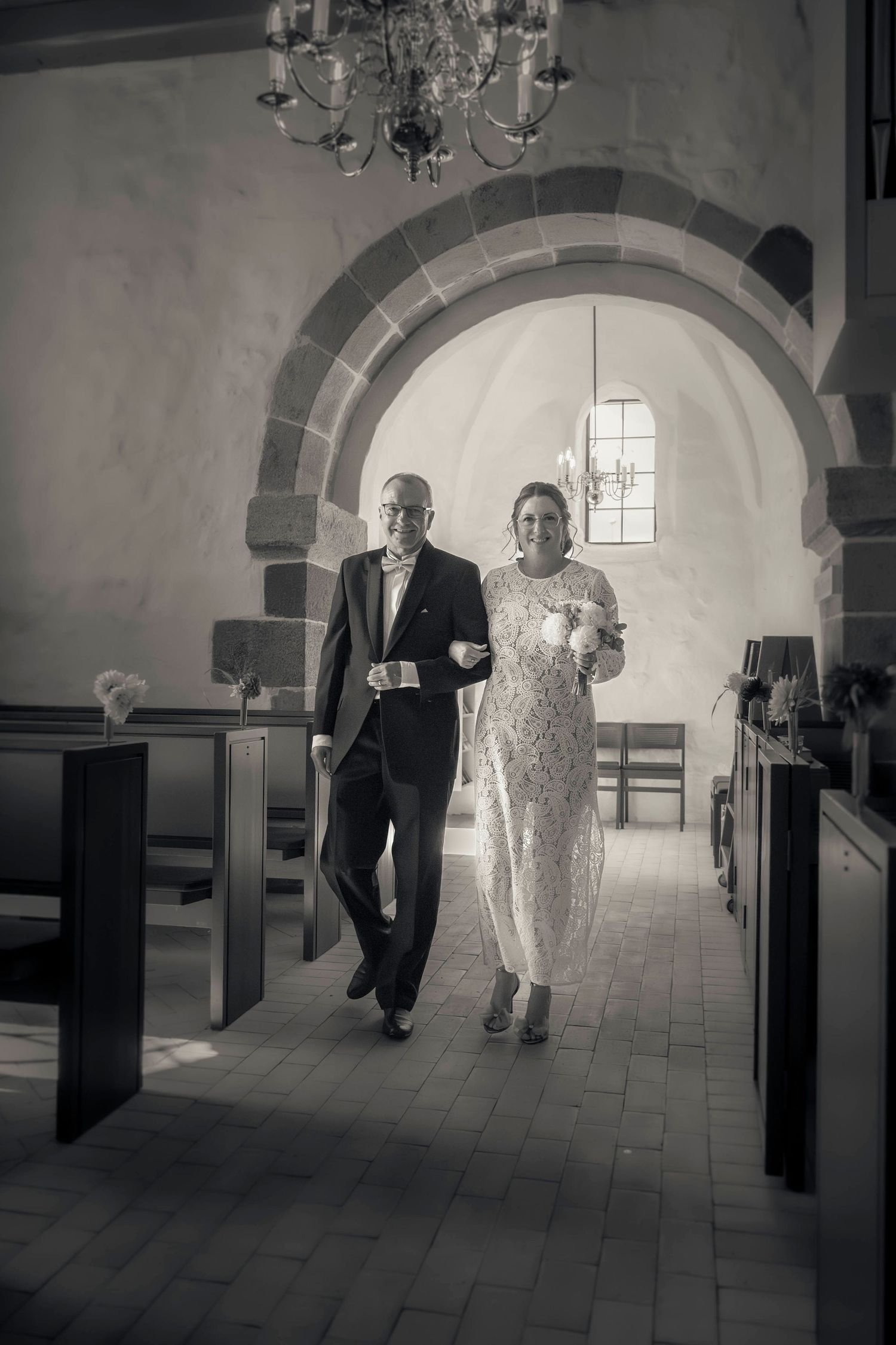 Black and white photo of a bride and groom walking down a church aisle during a wedding ceremony.
