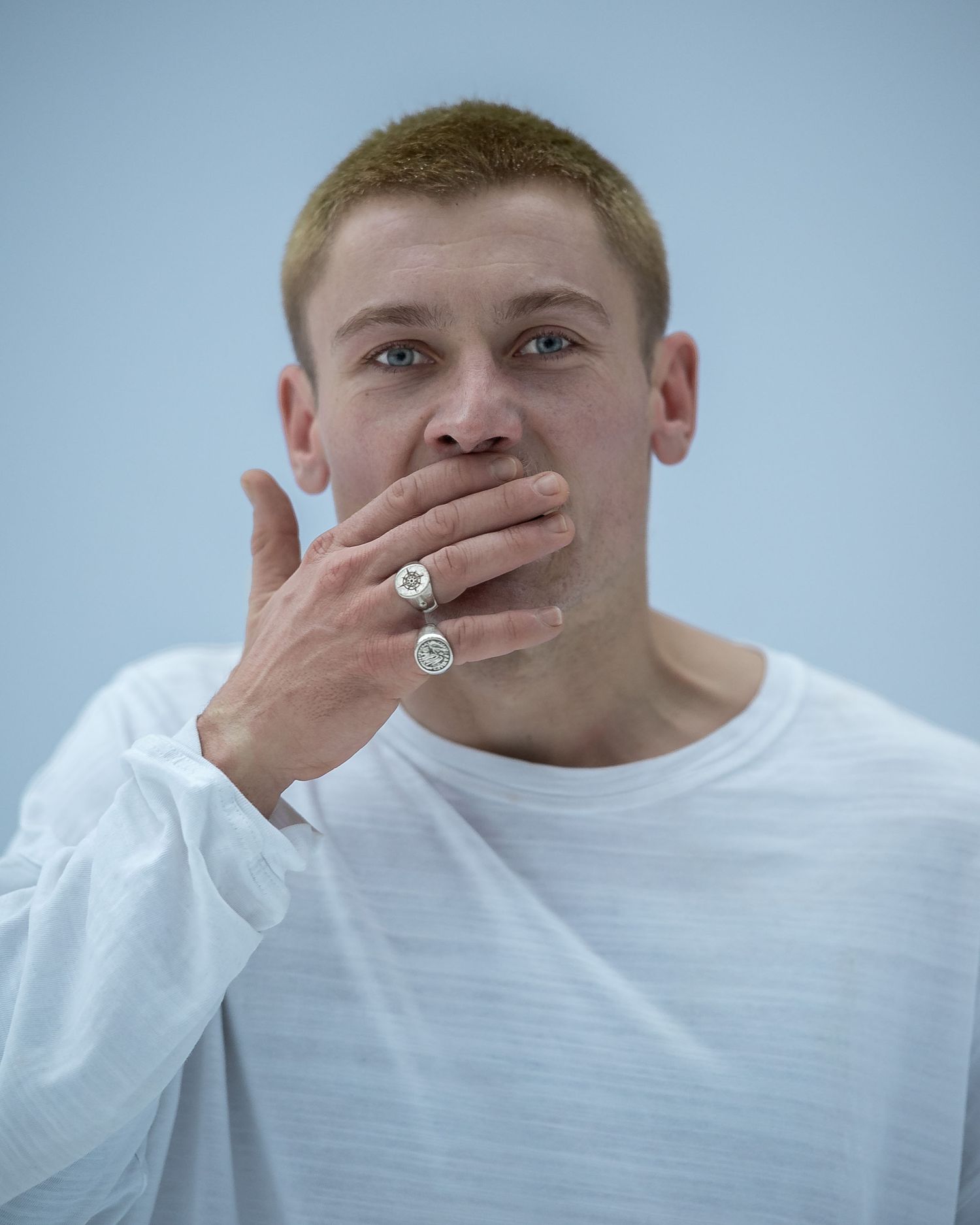 Young man in white shirt covering mouth with ringed hand.