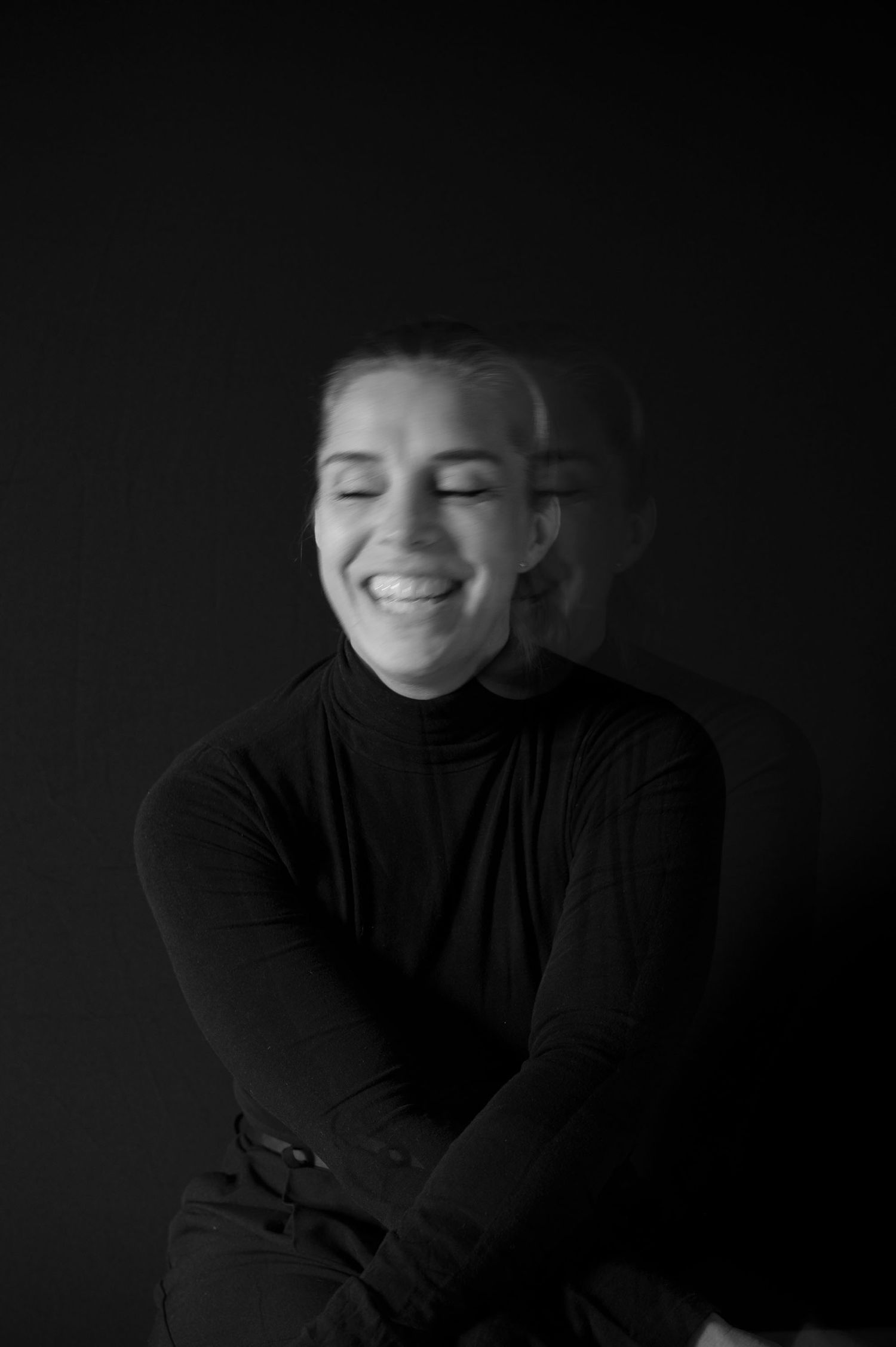 Smiling young woman with eyes closed wearing a black turtleneck, captured with motion blur effect.