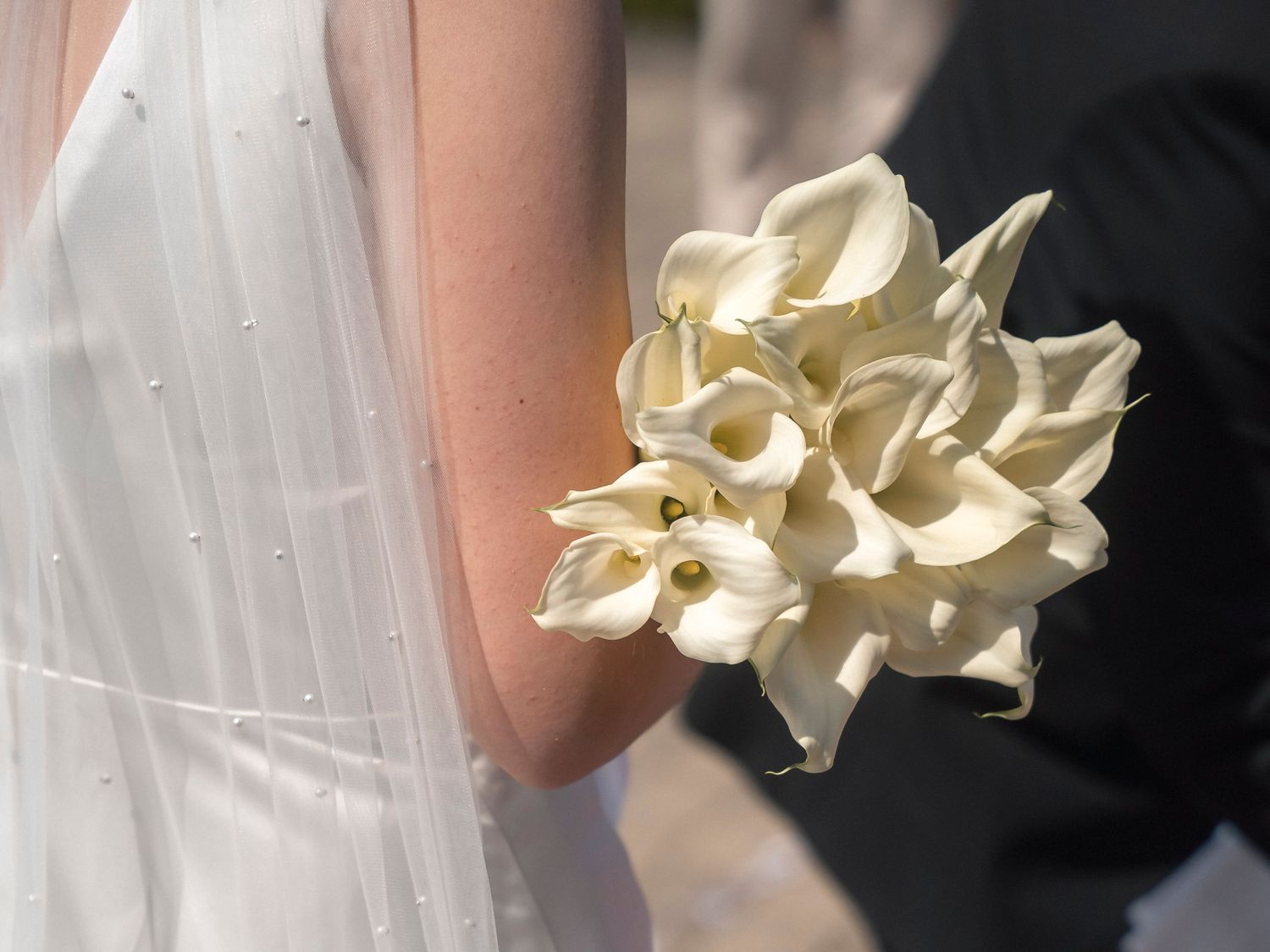 Bride holding a elegant white calla lily wedding bouquet while wearing a pearl-embellished white bridal gown.