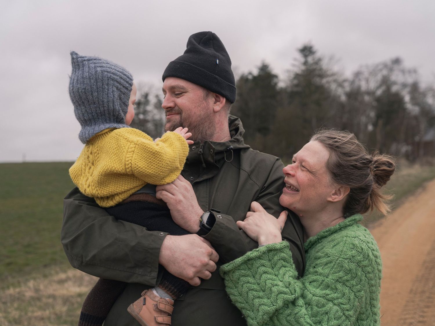 Happy family with a baby enjoying an outdoor walk on a cloudy day, wearing cozy knit sweaters and hats.