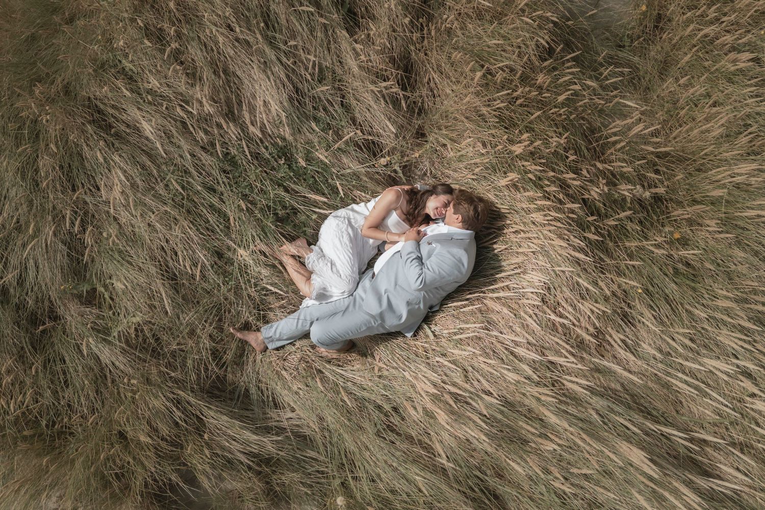 Wedding couple lying in tall coastal grass during outdoor photo session.
