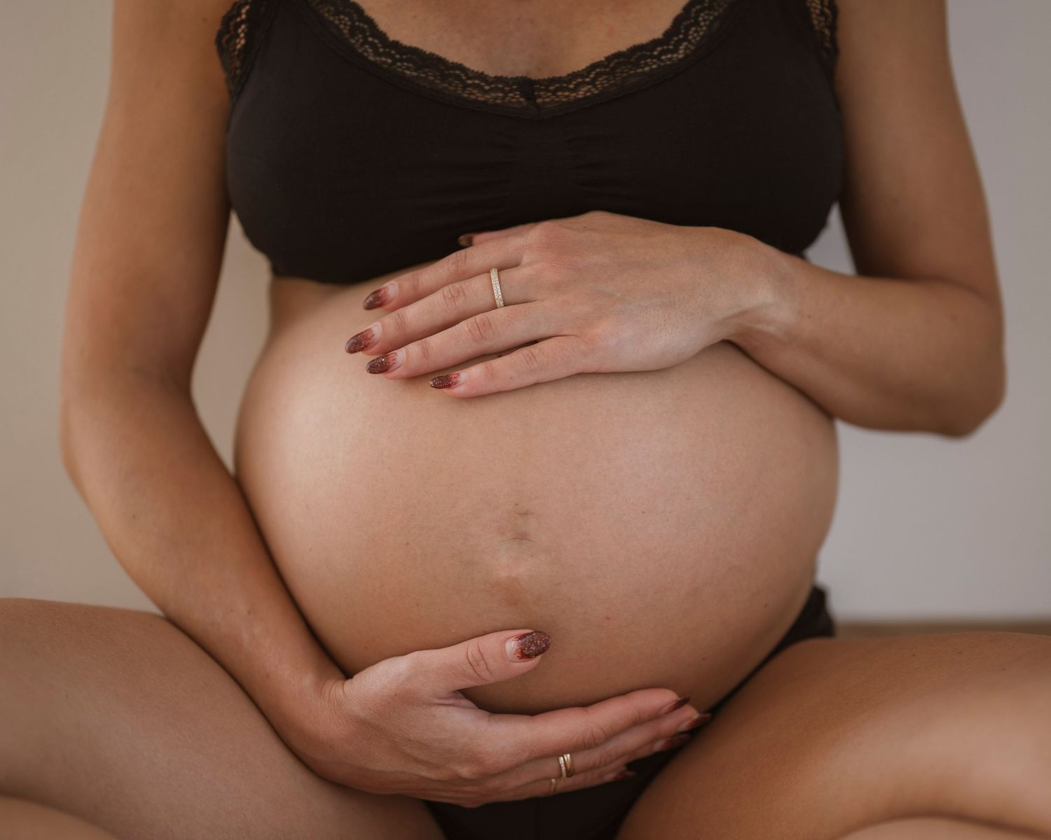 Pregnant woman in black lace bra cradling bare baby bump with both hands, maternity photography.