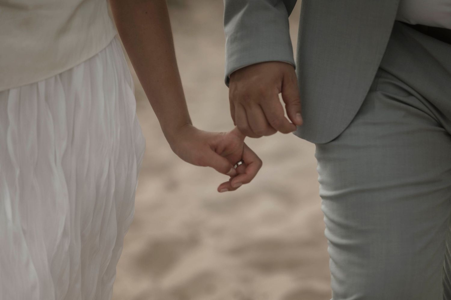 Close-up shot of a couple holding hands with bride in white dress and groom in gray suit.