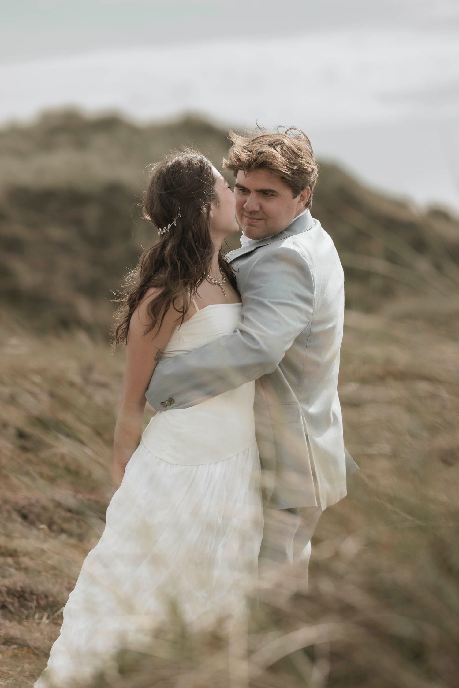 Intimate wedding portrait of couple embracing on windswept coastal hillside.