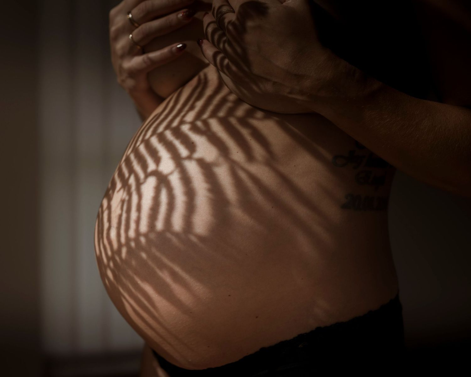 Close-up of a pregnant belly with beautiful leaf shadows cast across the skin in warm light.