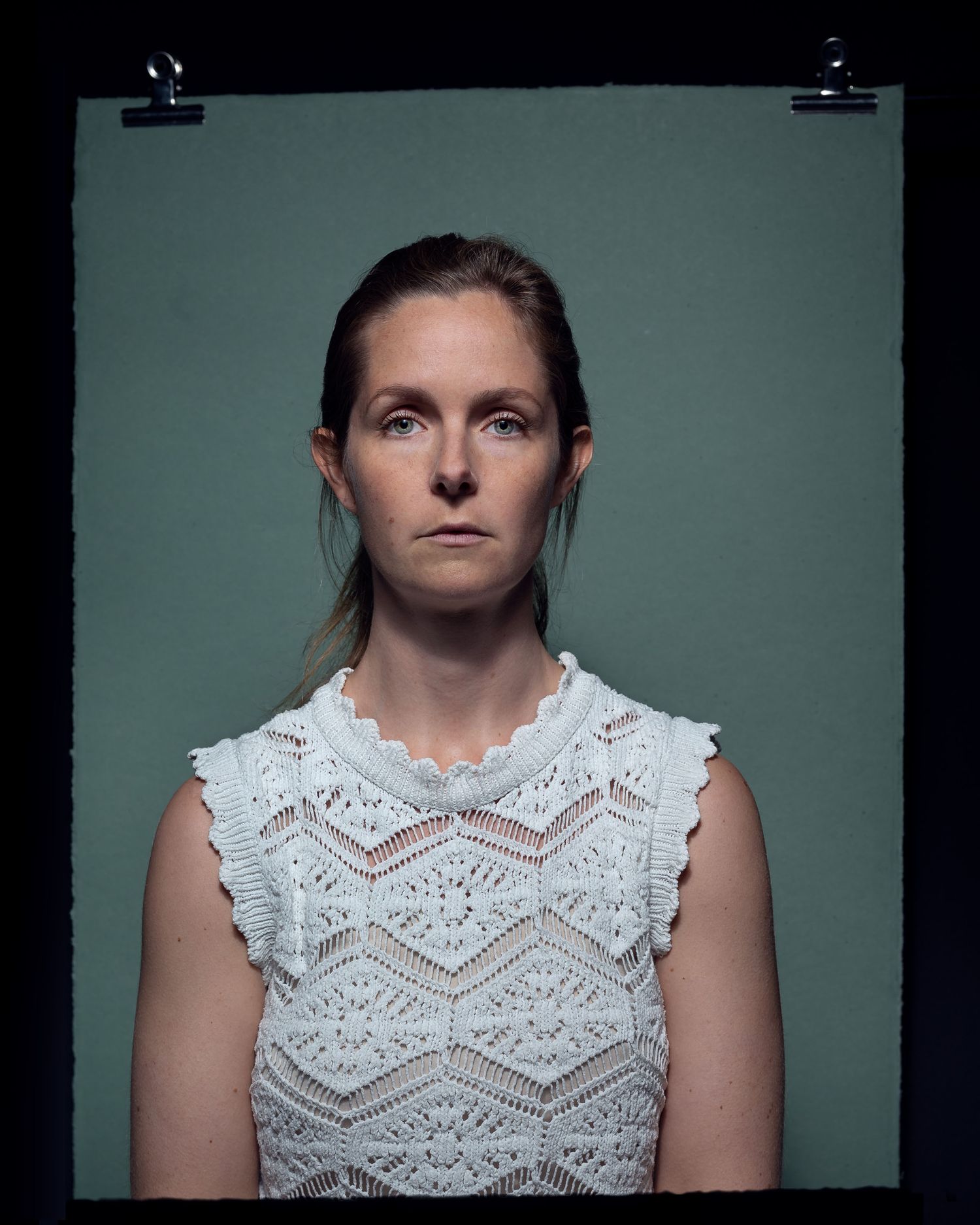 Woman in white lace top posing for serious portrait photo.