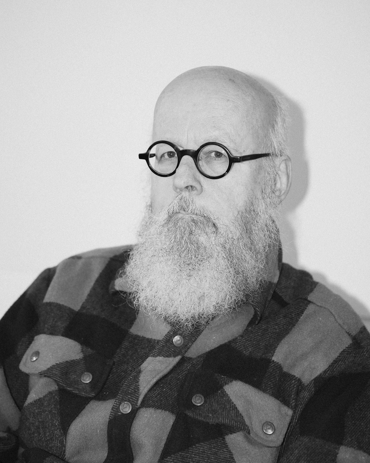 Black and white portrait of a bald man with a white beard wearing round glasses and a plaid flannel shirt.