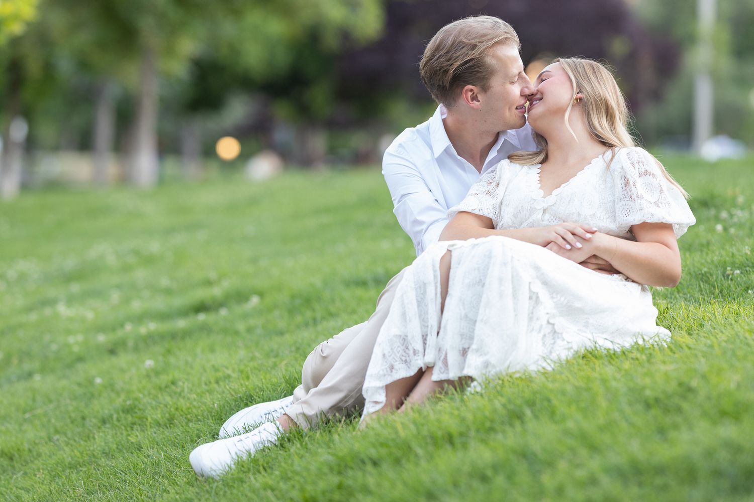 Couple in white outfits shares playful moments on grassy hillside.