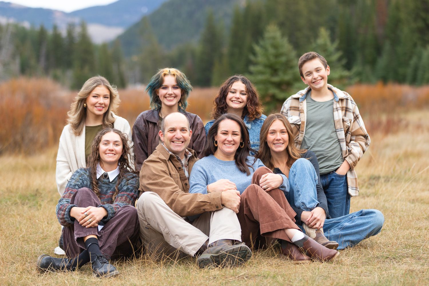 A family relaxes together in a grassy field in a Utah Canyon with an evergreen forest in the background.