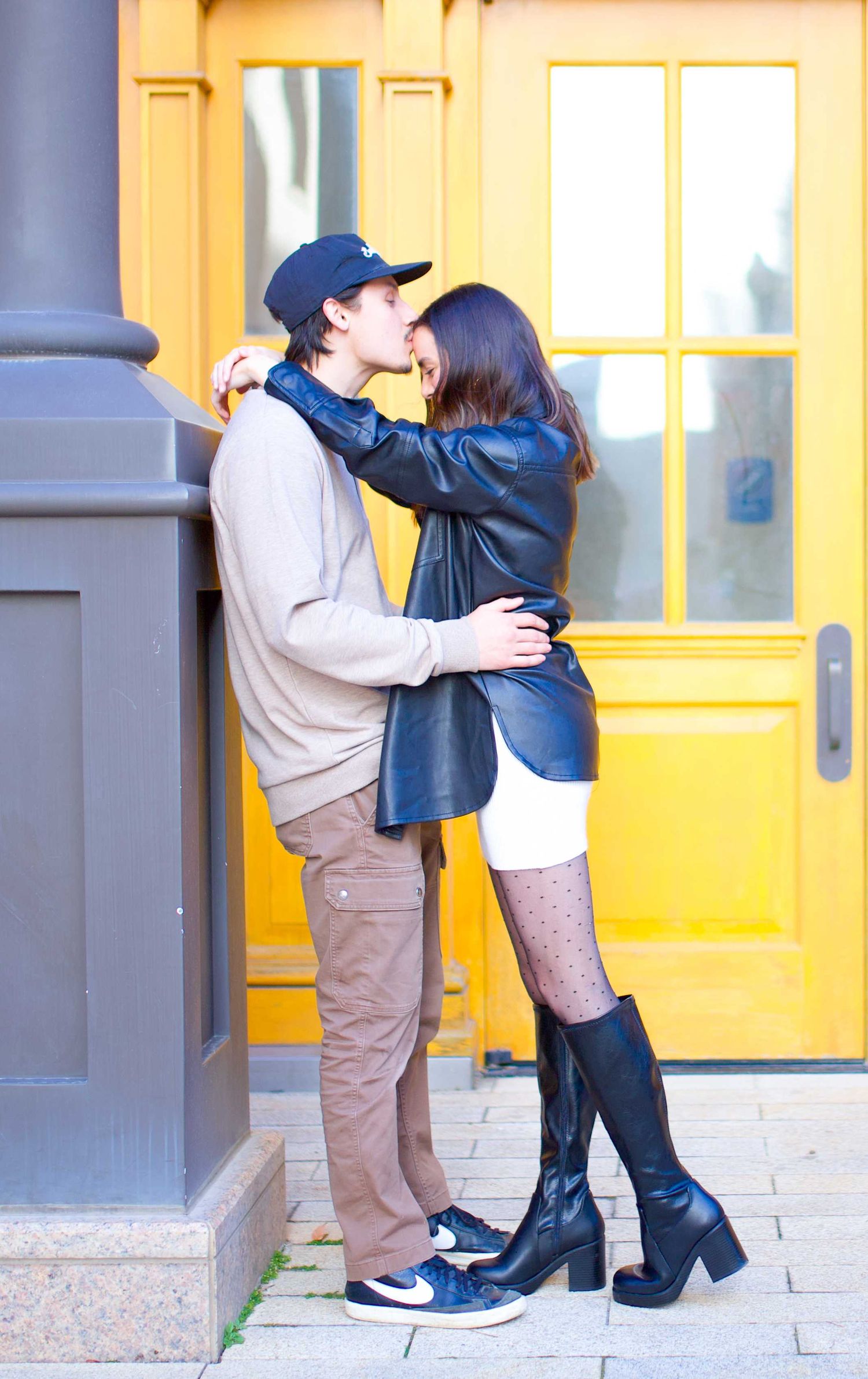 Couple sharing a romantic kiss in front of a yellow door with colonial architecture.